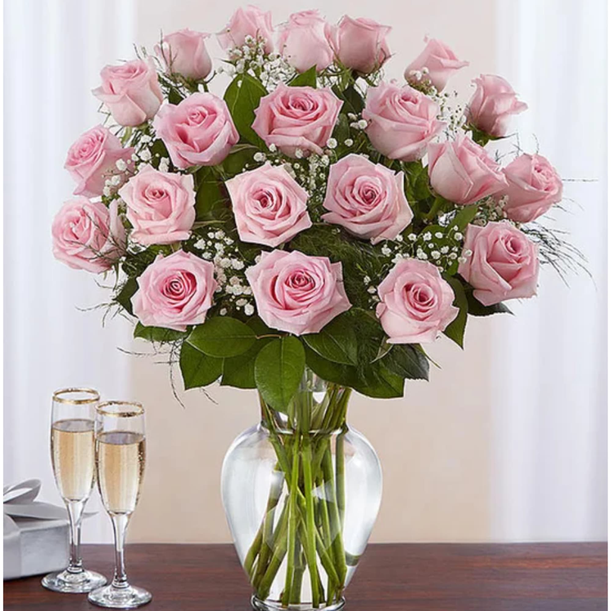 Pink roses arranged in a clear glass vase with two champagne flutes nearby
