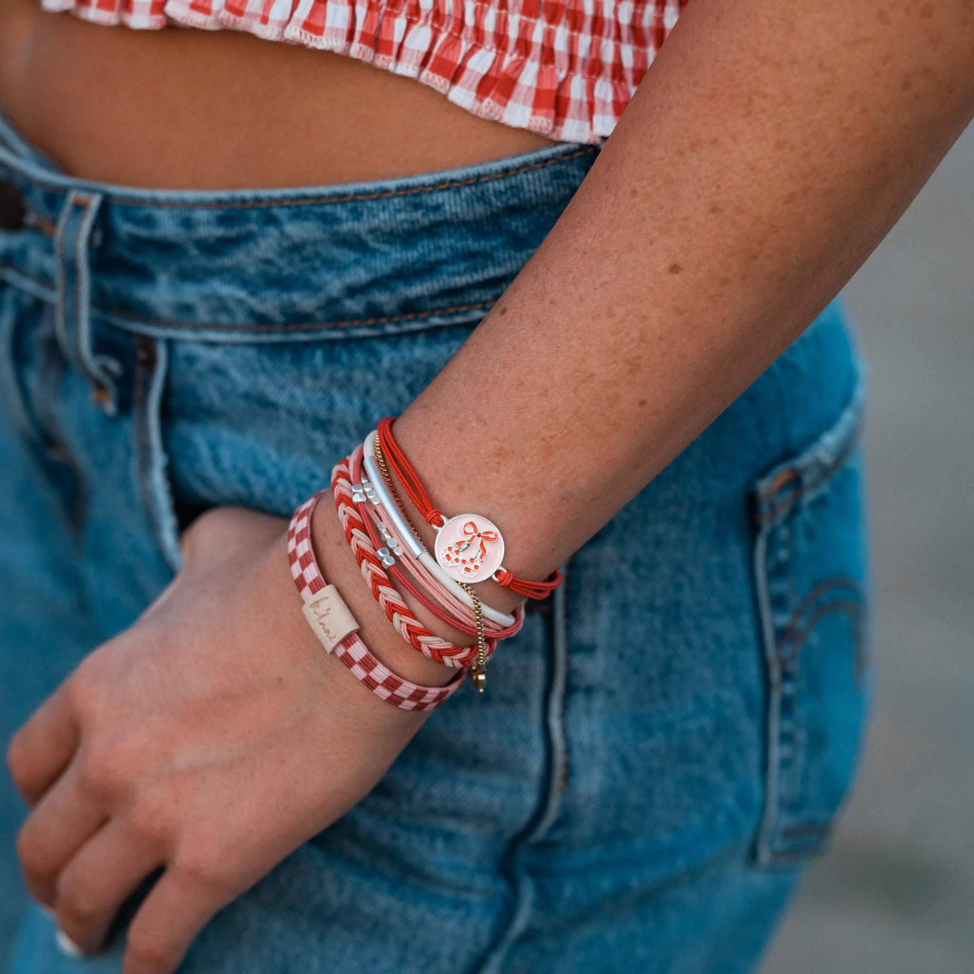 Person wearing stacked red and pink bracelets with a small charm