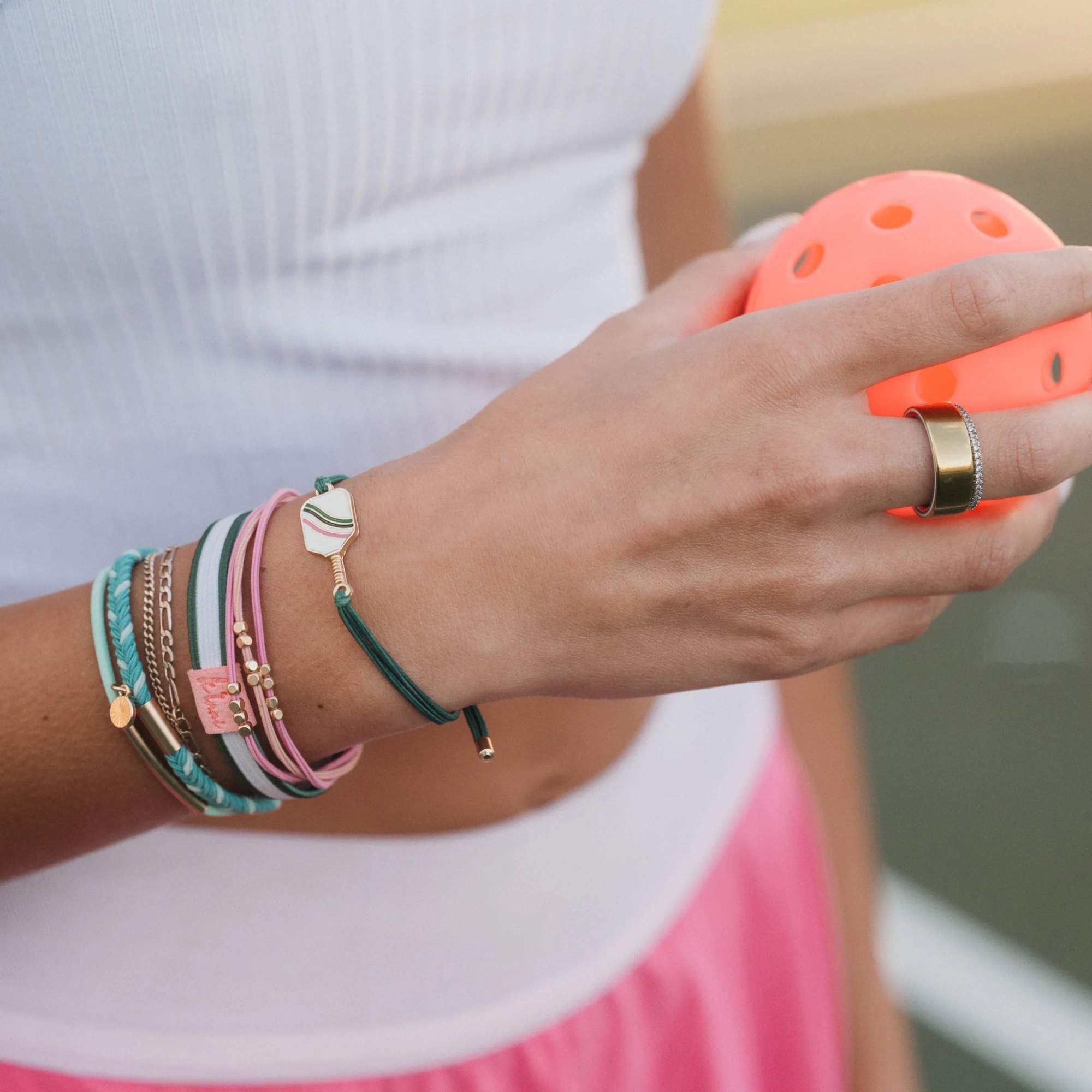 Person wearing stacked bracelets and holding a bright orange perforated ball