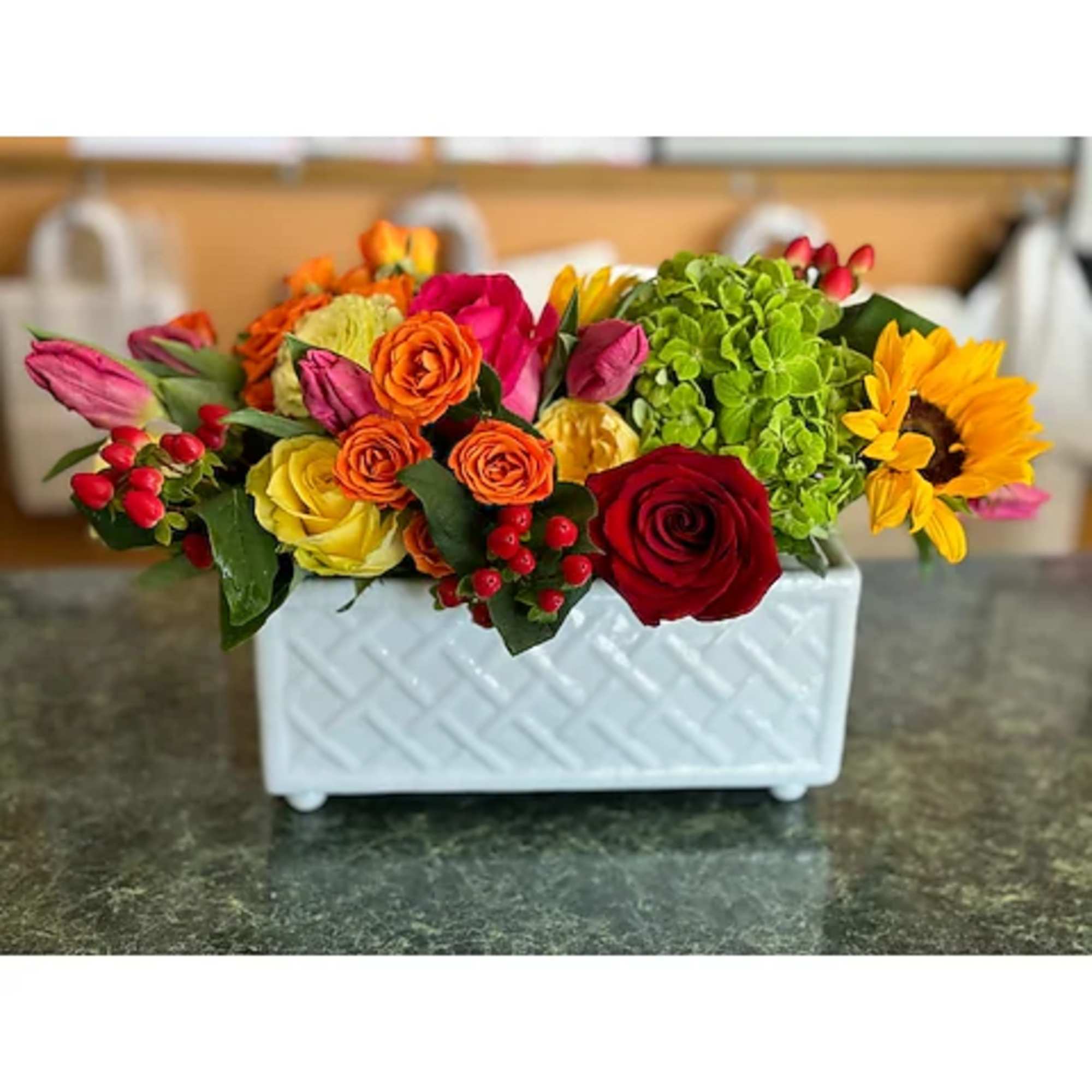 Mixed bouquet in a white rectangular vase with roses, tulips, hydrangea, and a sunflower