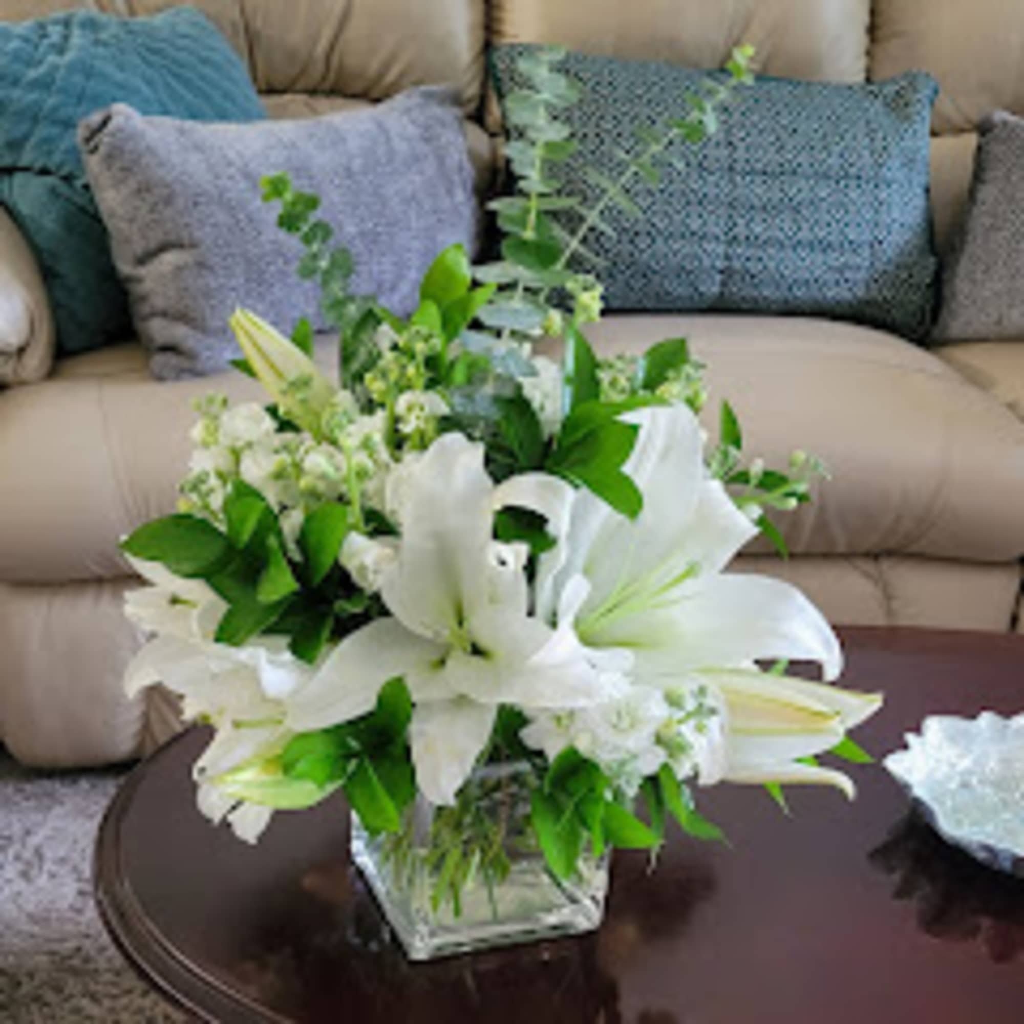 White lilies arranged in a clear glass vase on a coffee table