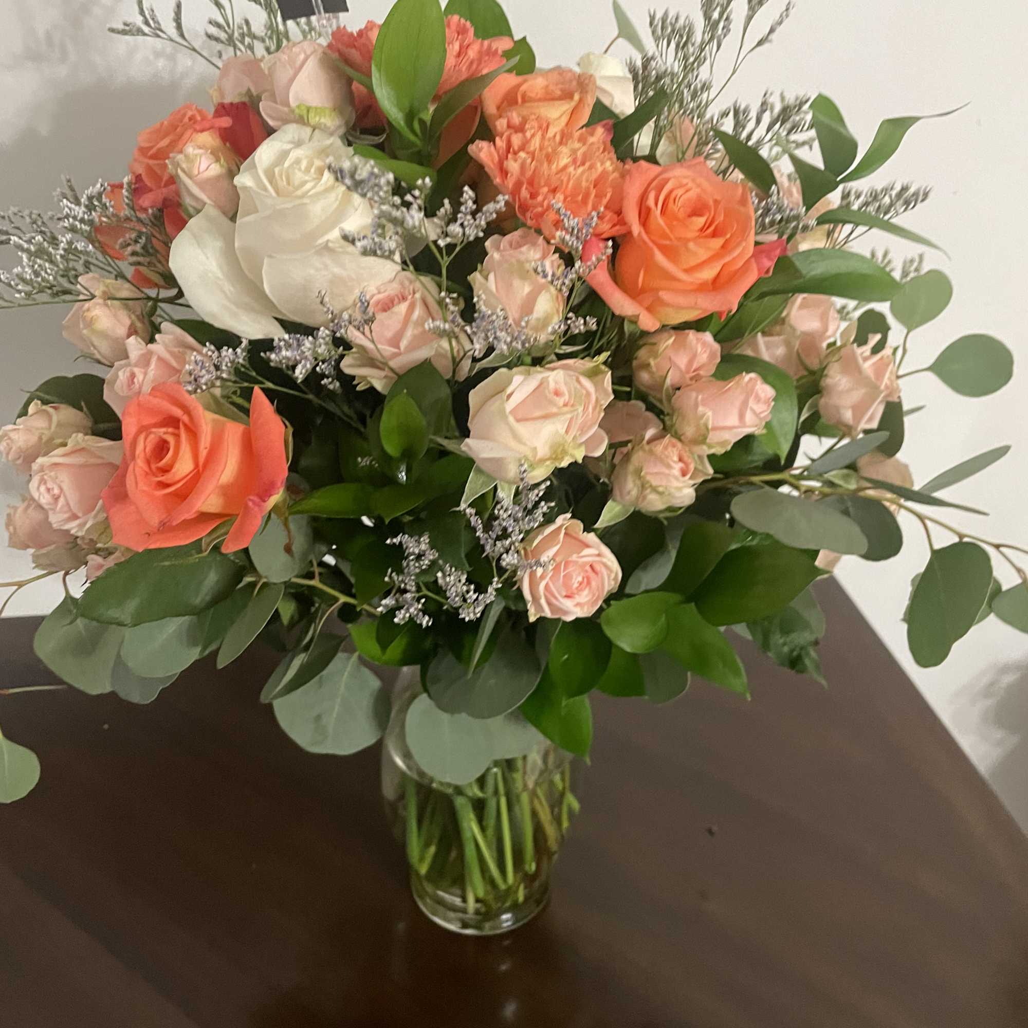 Mixed bouquet of peach, pink, and white roses in a clear glass vase