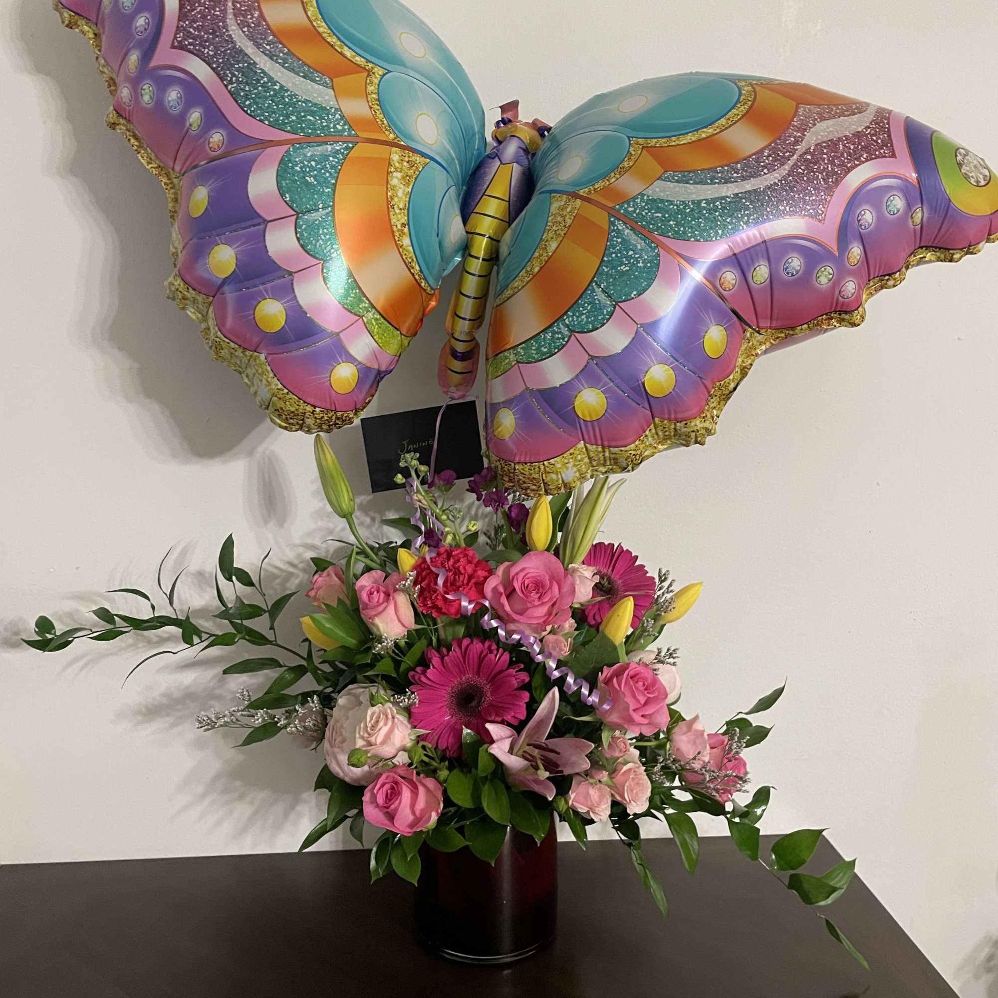 Pink floral arrangement with a colorful butterfly balloon in a vase