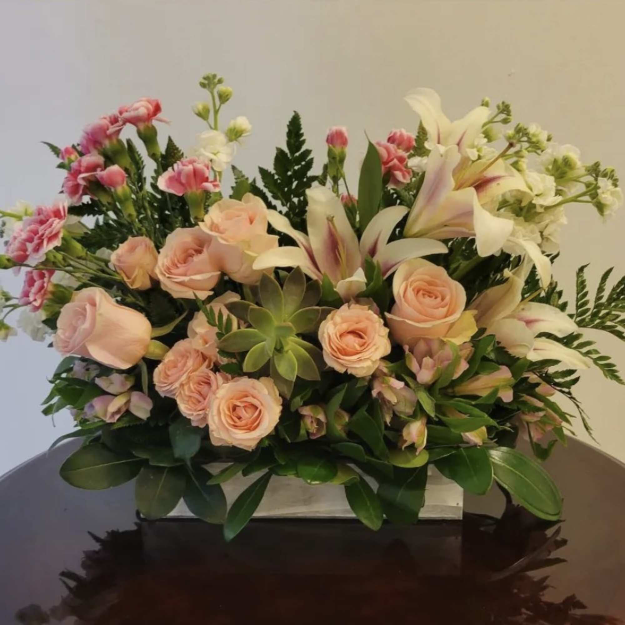 Peach roses and white lilies arranged with pink carnations in a low container