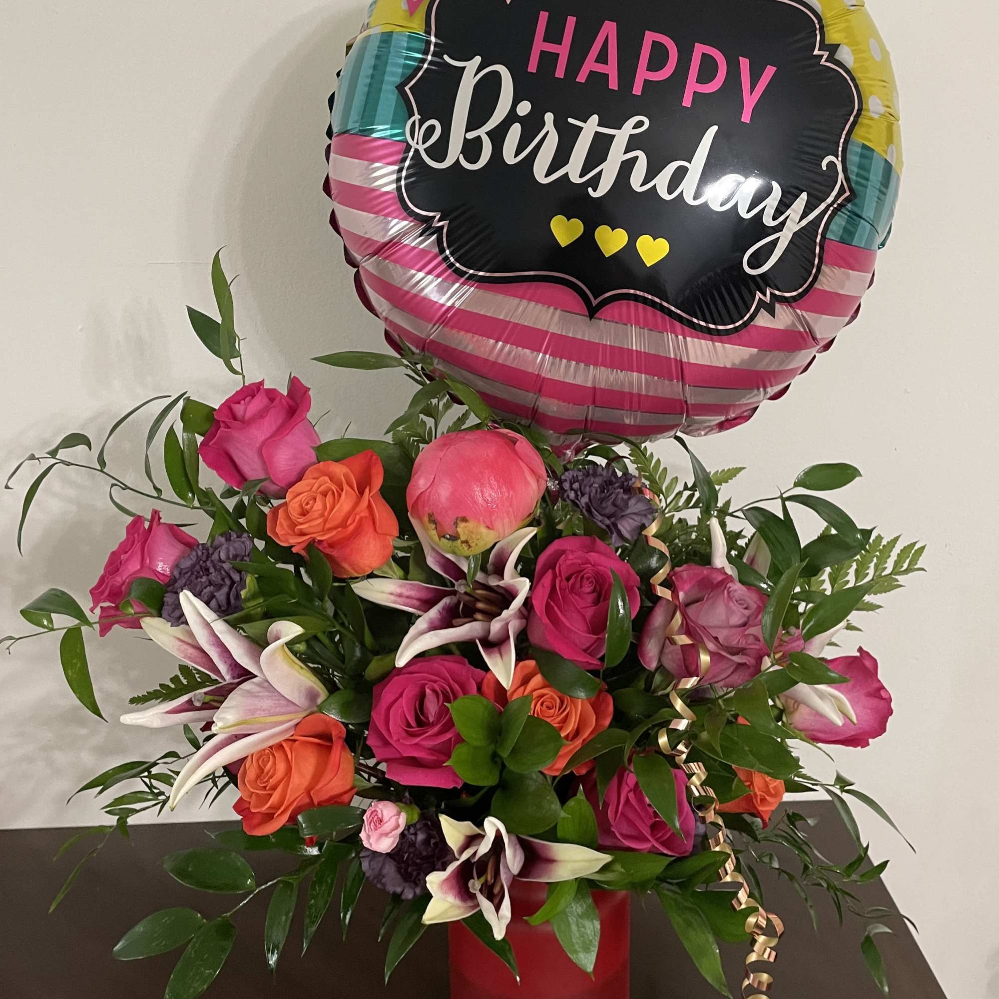 Birthday balloon above a colorful rose arrangement in a red vase