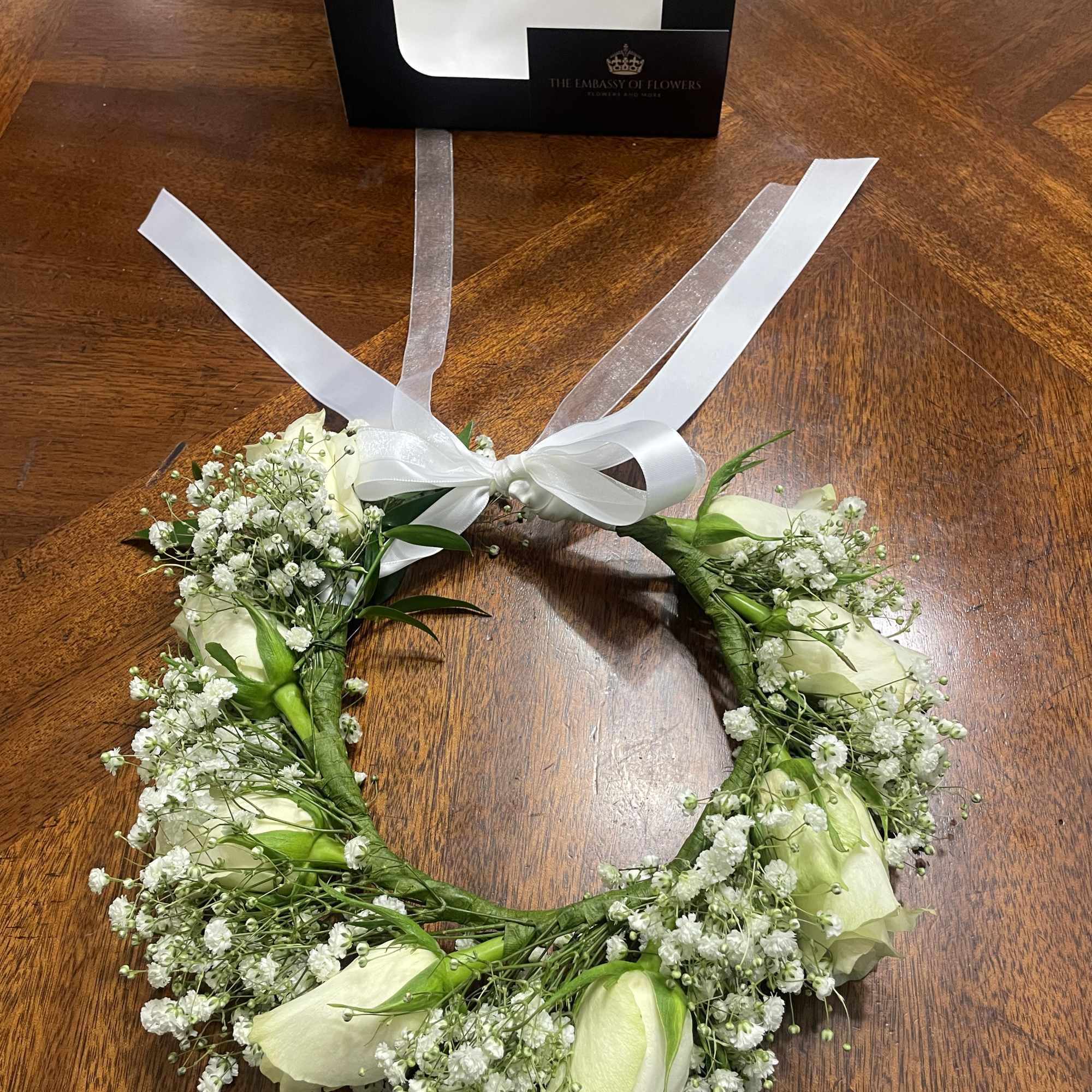 White floral wreath with ribbon ties on a wooden table