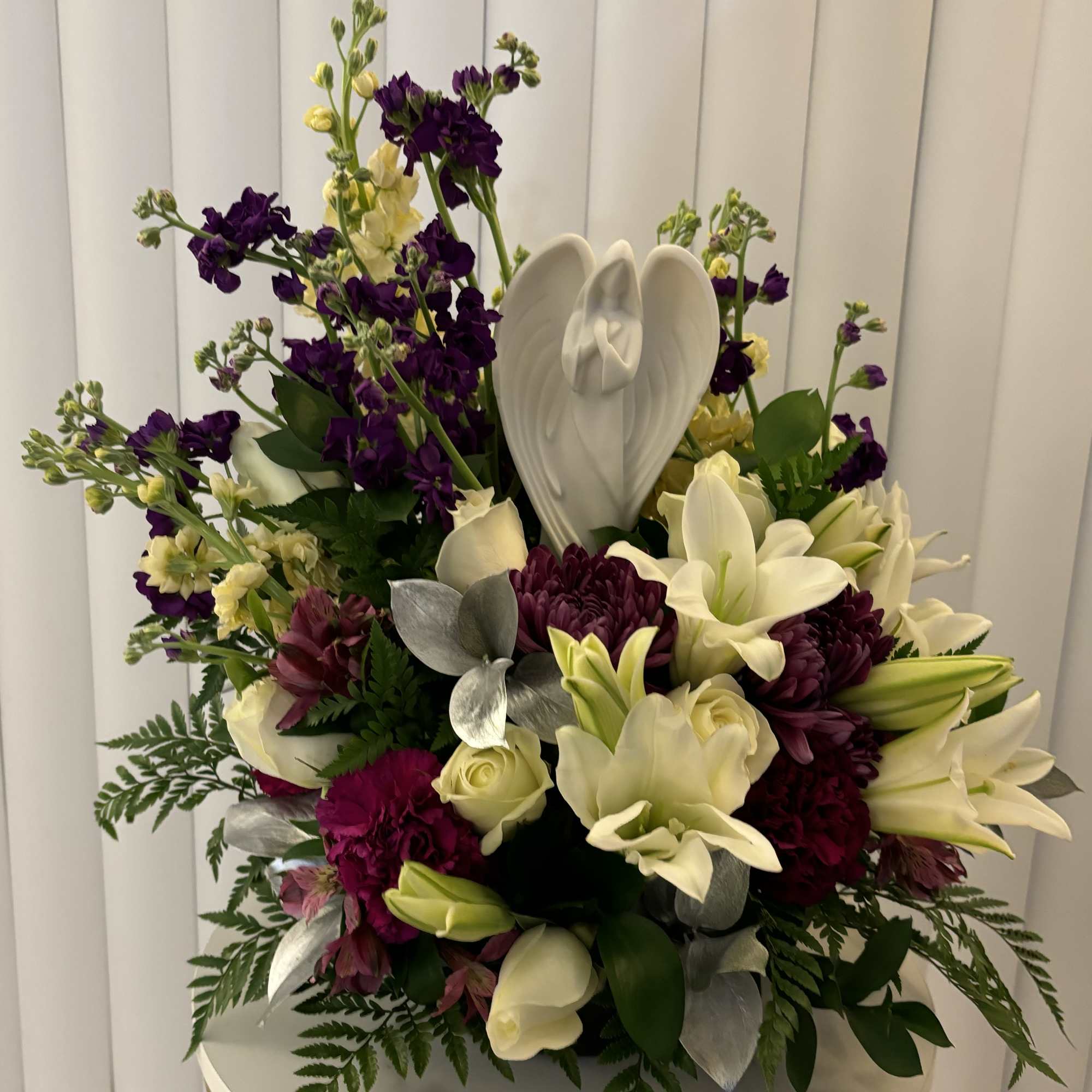 White lilies and purple flowers arranged with a white angel figurine