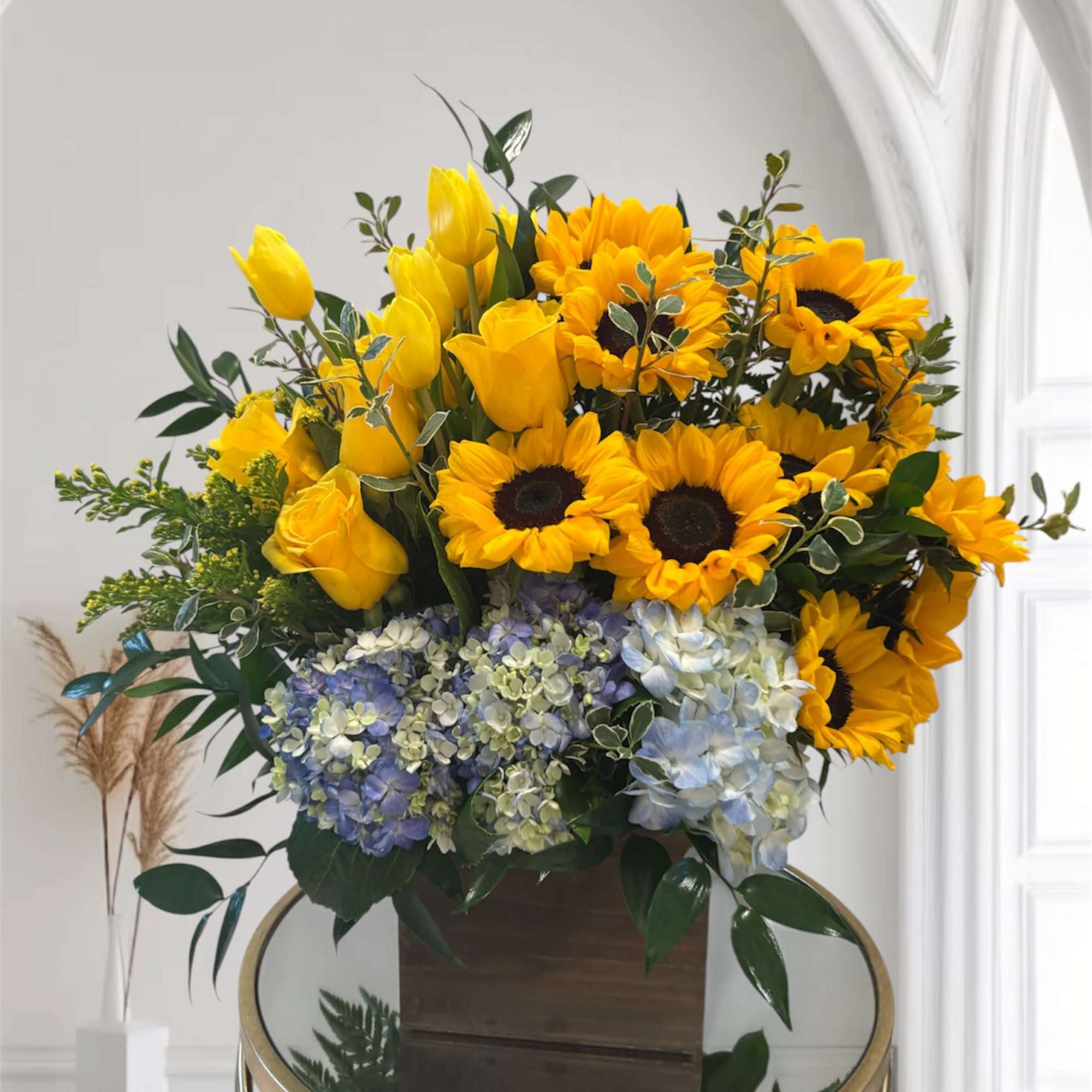 Yellow tulips, sunflowers, and blue hydrangeas in a wooden box