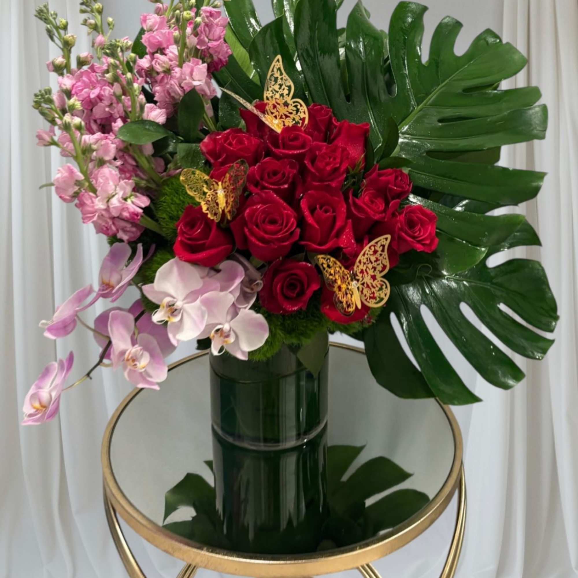 Bouquet of red roses, pink orchids, and pink stock in a dark vase