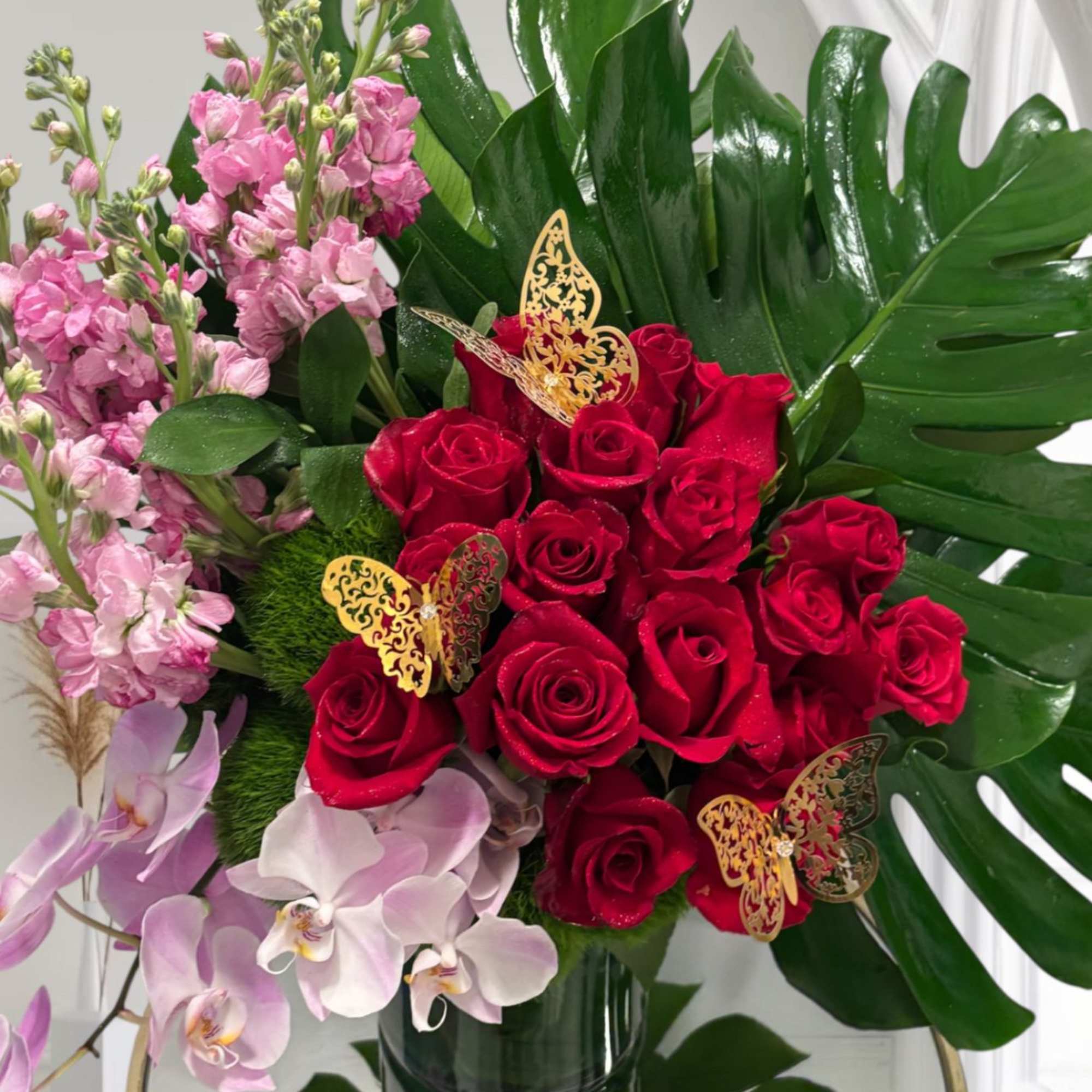Red roses with pink orchids and stock in a glass vase