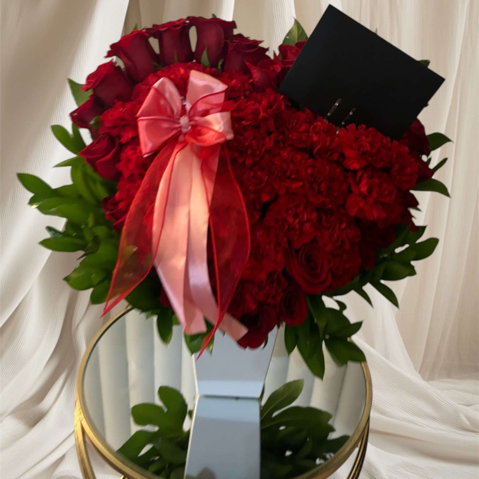 Red rose and carnation arrangement with a pink ribbon in a white vase
