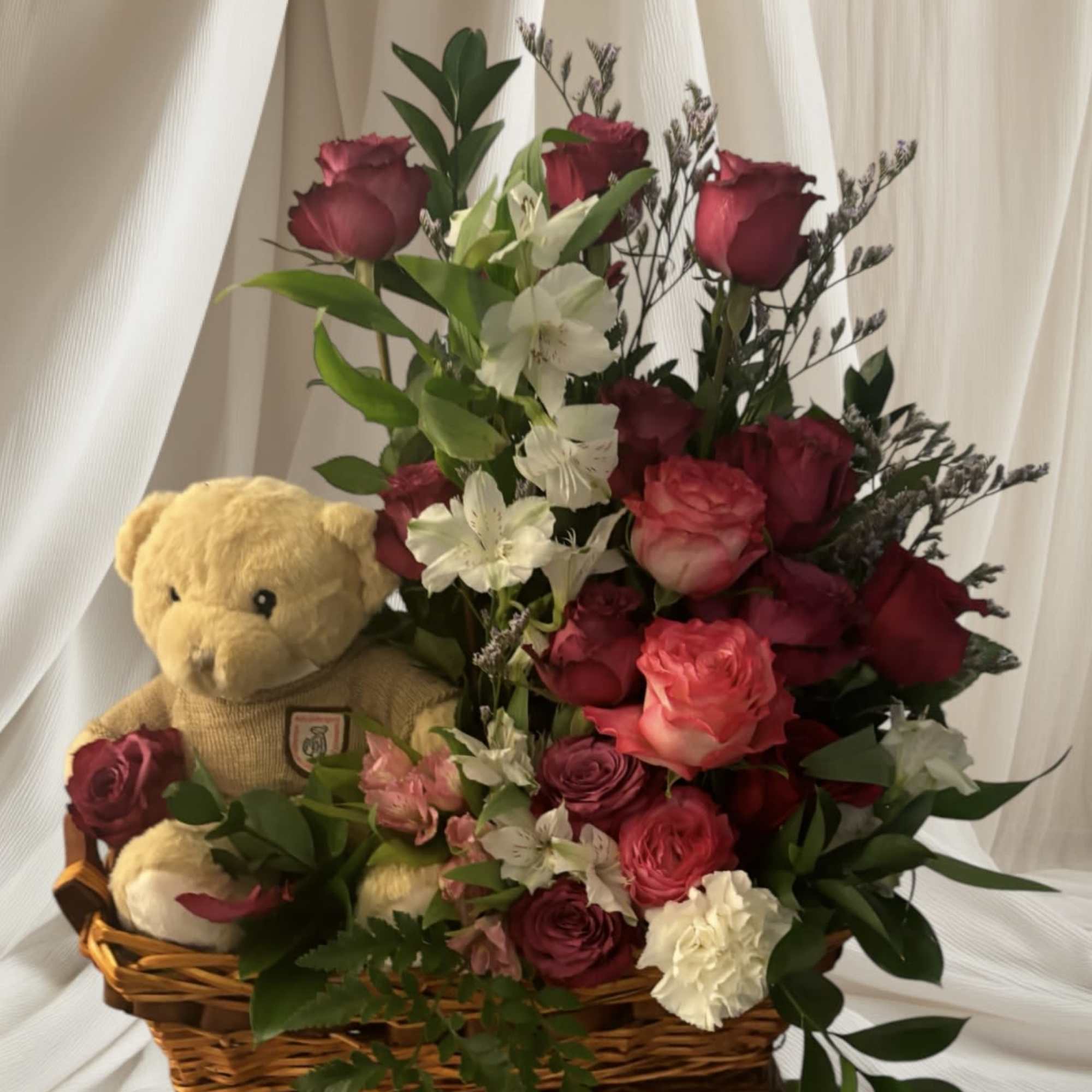 Basket arrangement of red roses and white flowers with a teddy bear