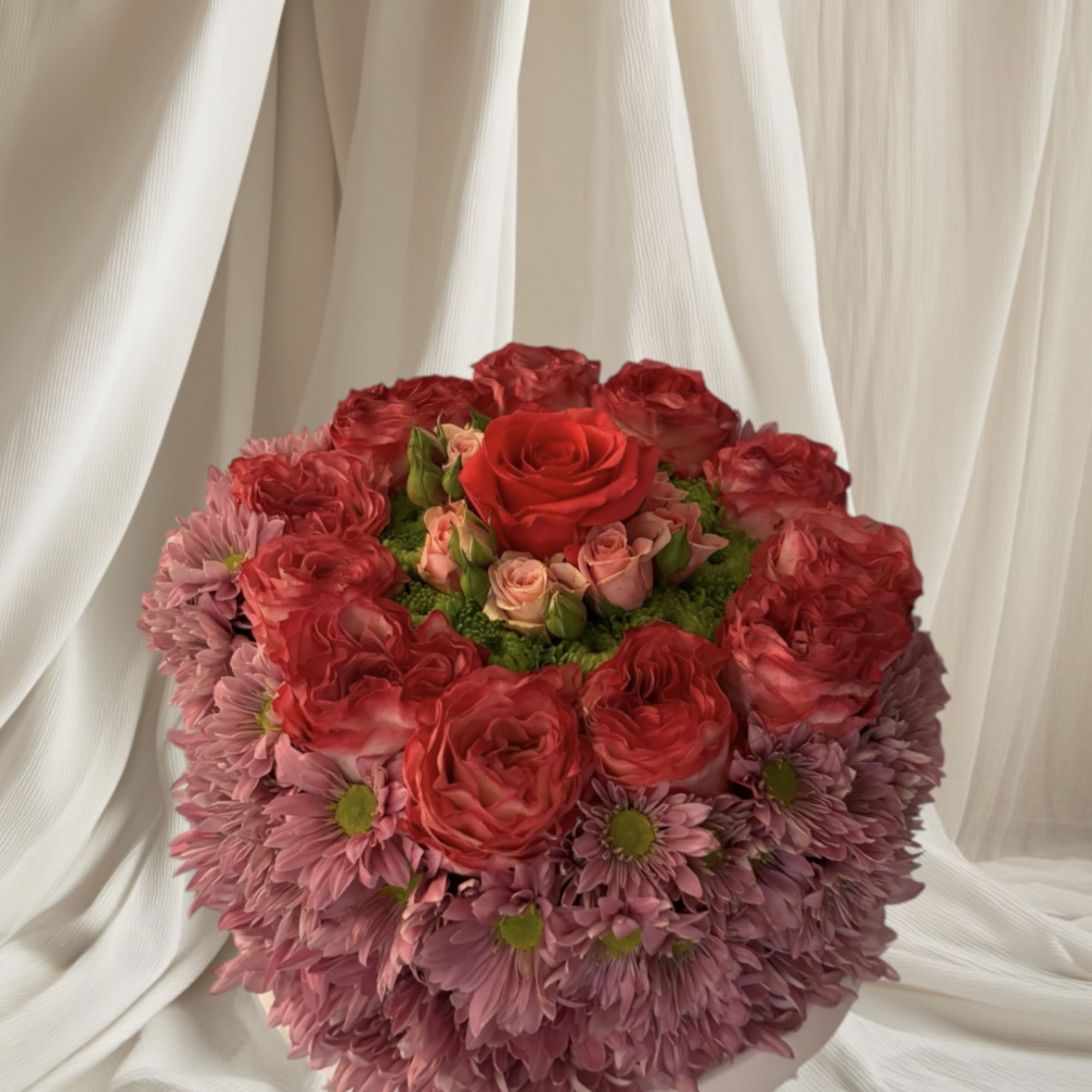 Round bouquet of pink and red flowers in a white hatbox