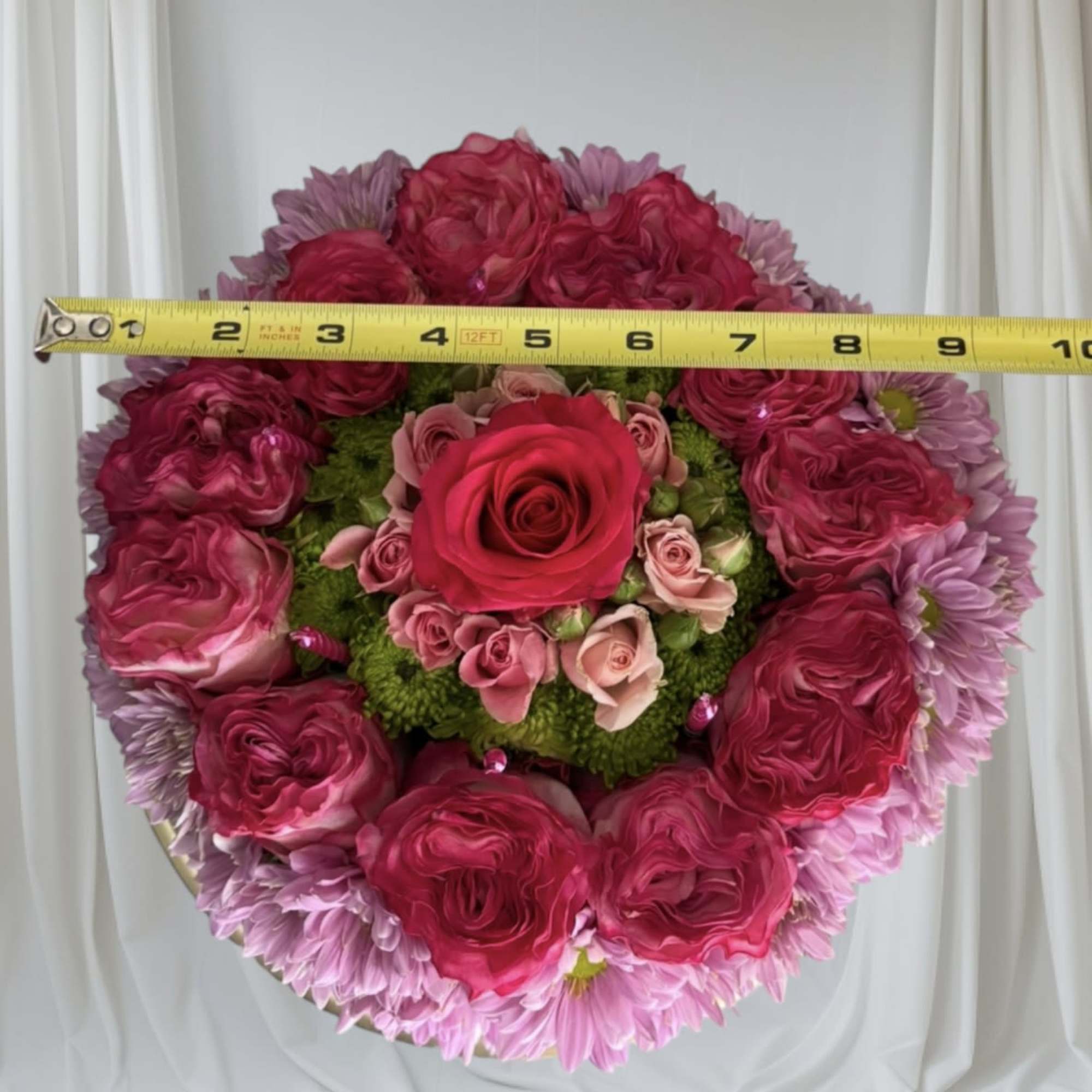 Round bouquet of pink roses and lavender daisies with a tape measure across the top