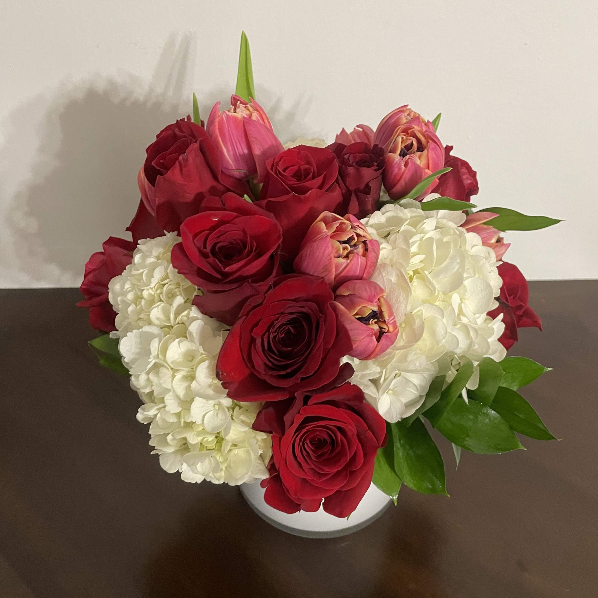 Red roses and pink tulips arranged with white hydrangeas in a white vase