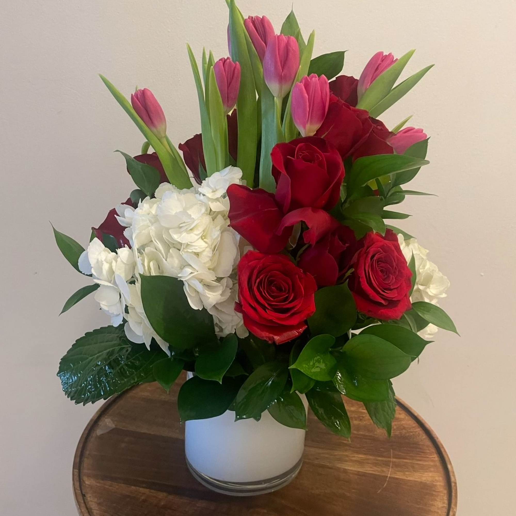 Bouquet of red roses, pink tulips, and white hydrangeas in a white vase