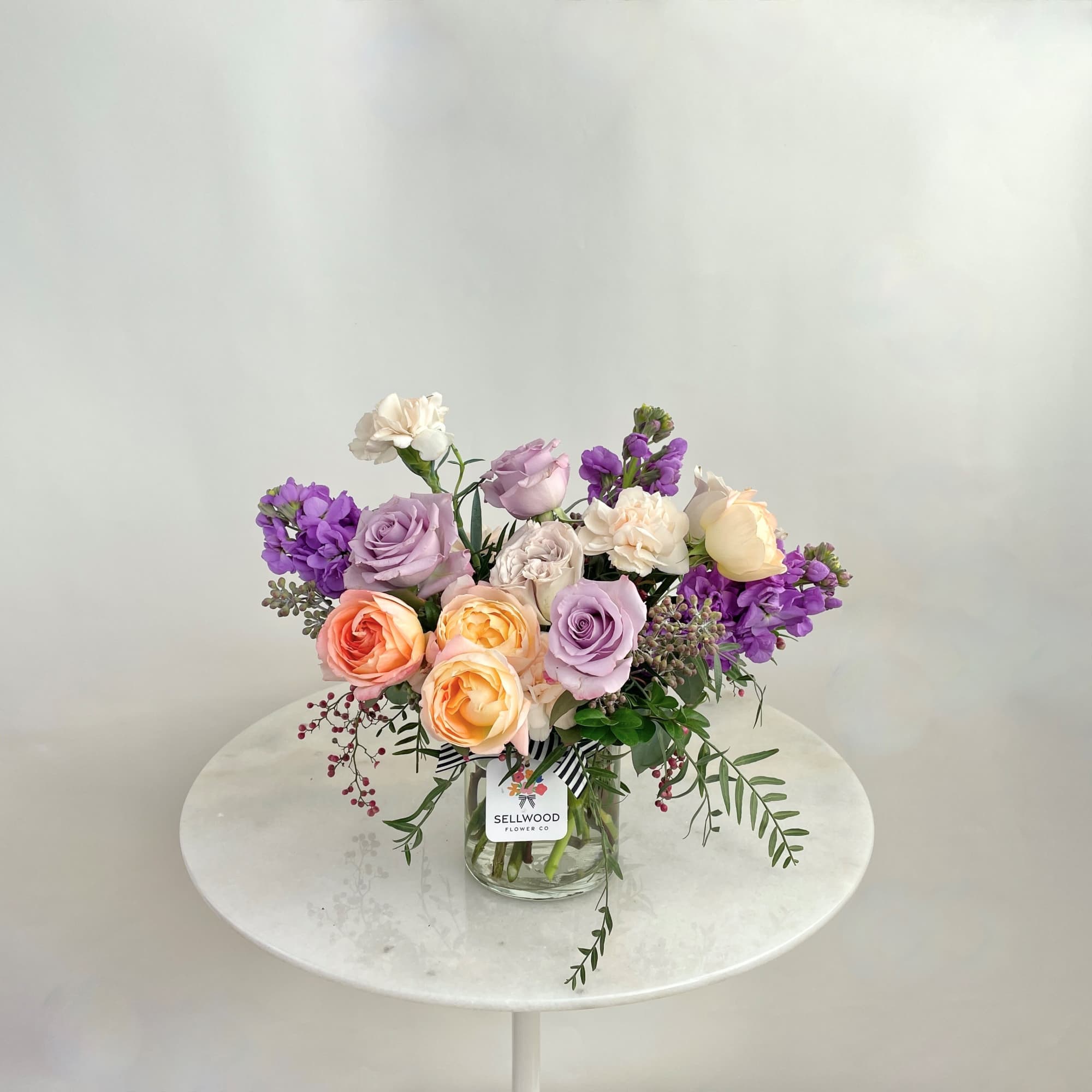 Mixed pastel roses and purple flowers in a clear glass vase