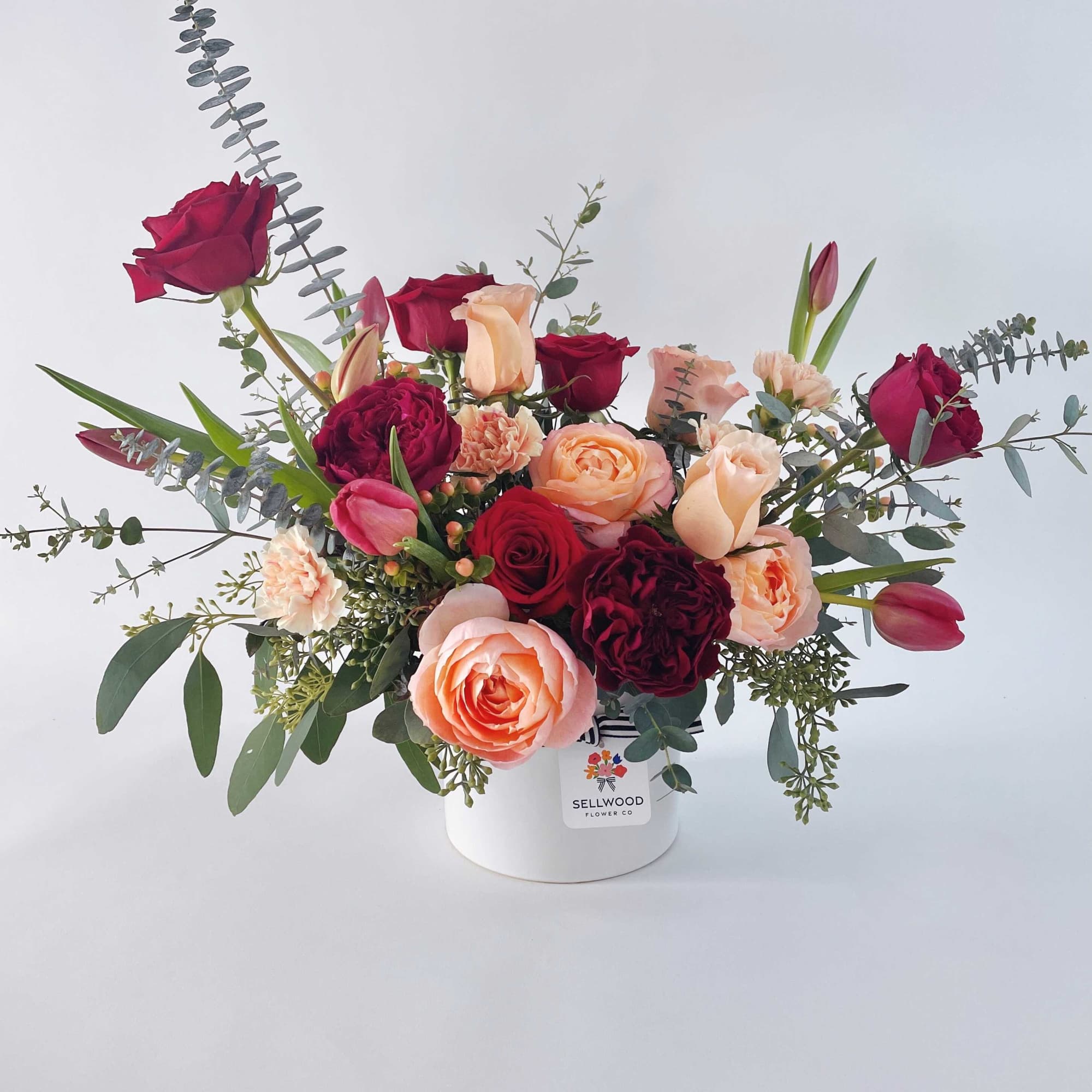 Mixed roses and tulips arranged in a white hat box