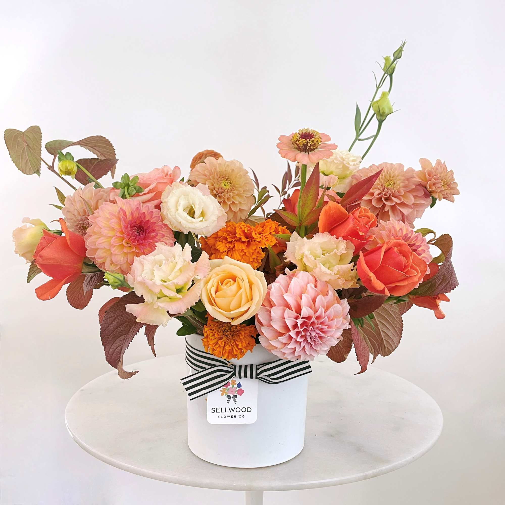 Mixed bouquet of peach, pink, white, and orange flowers in a white box