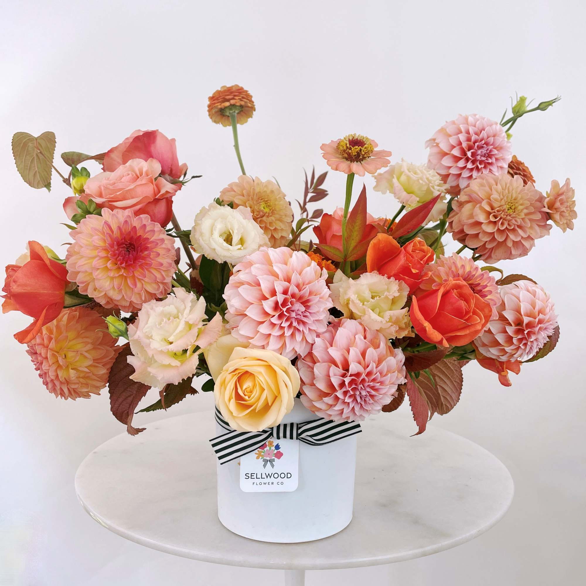 Peach and pink flowers arranged in a white hatbox with a striped ribbon