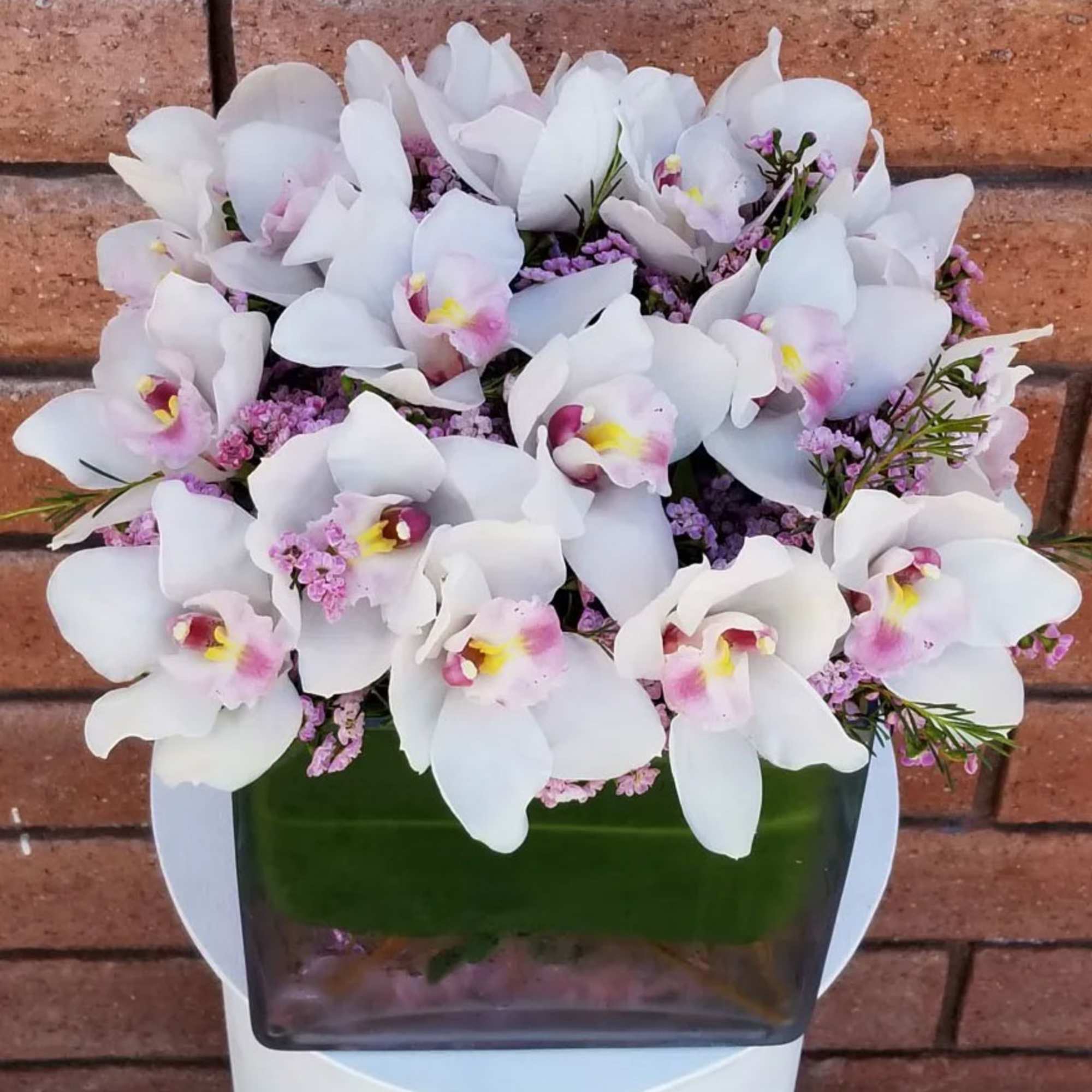 White orchids arranged in a green glass vase with pink filler flowers