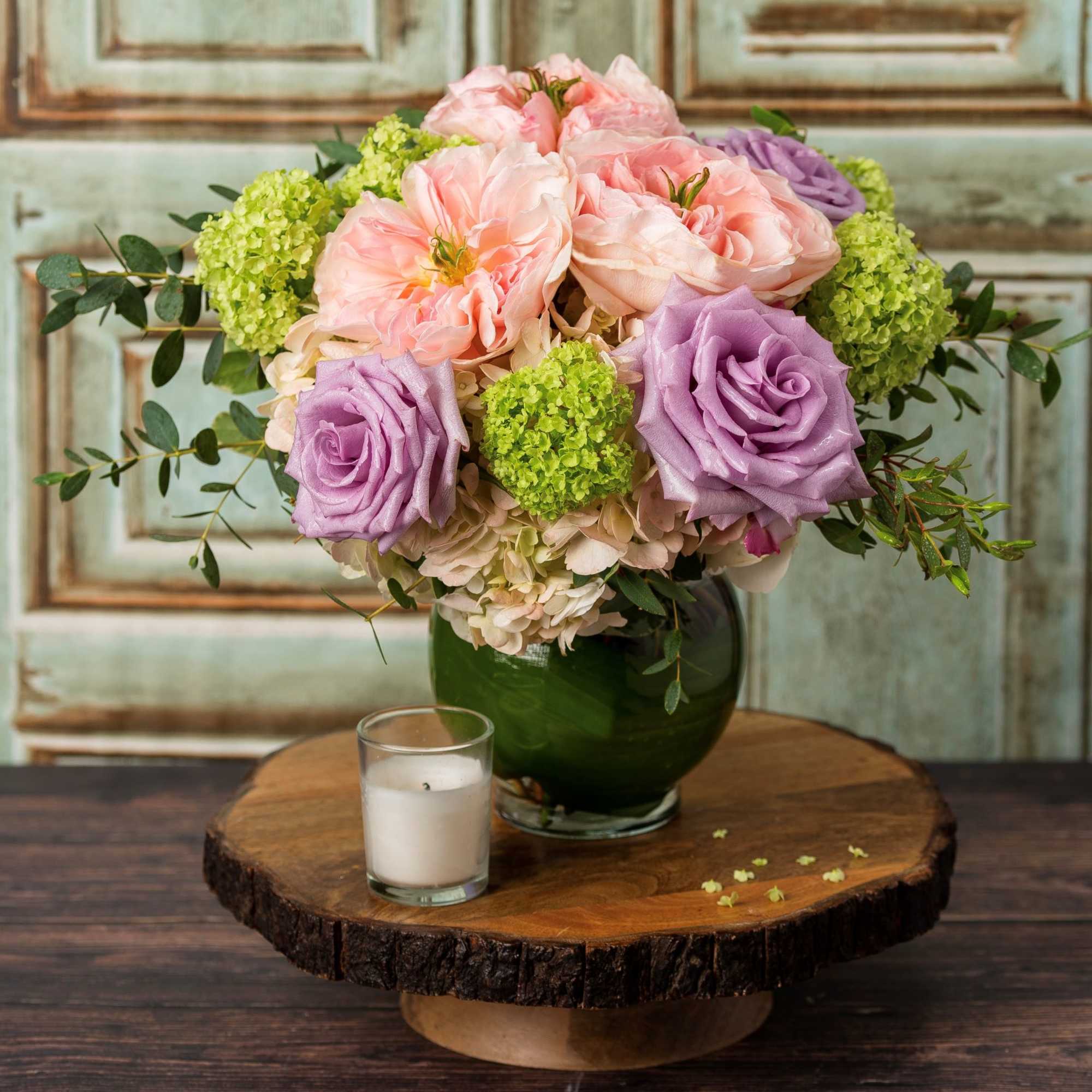 Pink and lavender roses in a green glass vase with a candle