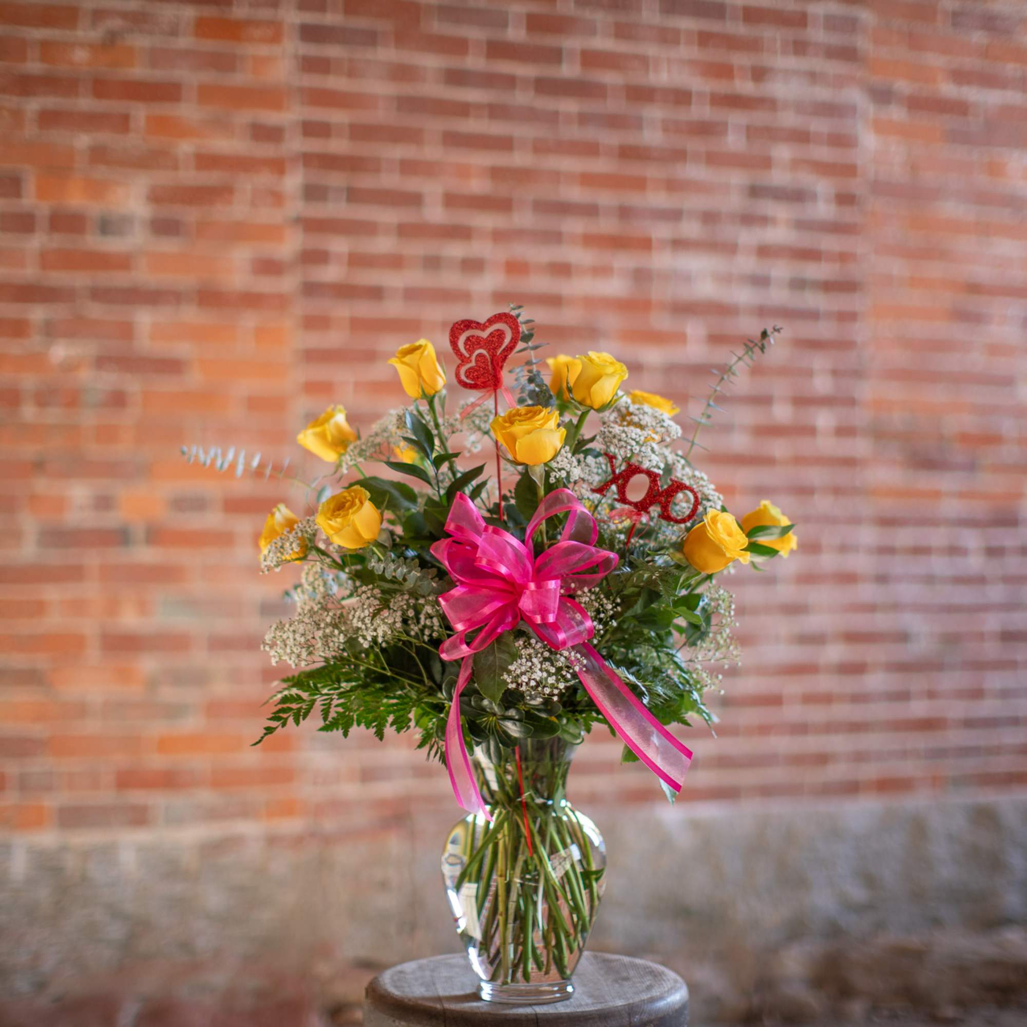 Yellow roses in a clear glass vase with a pink ribbon