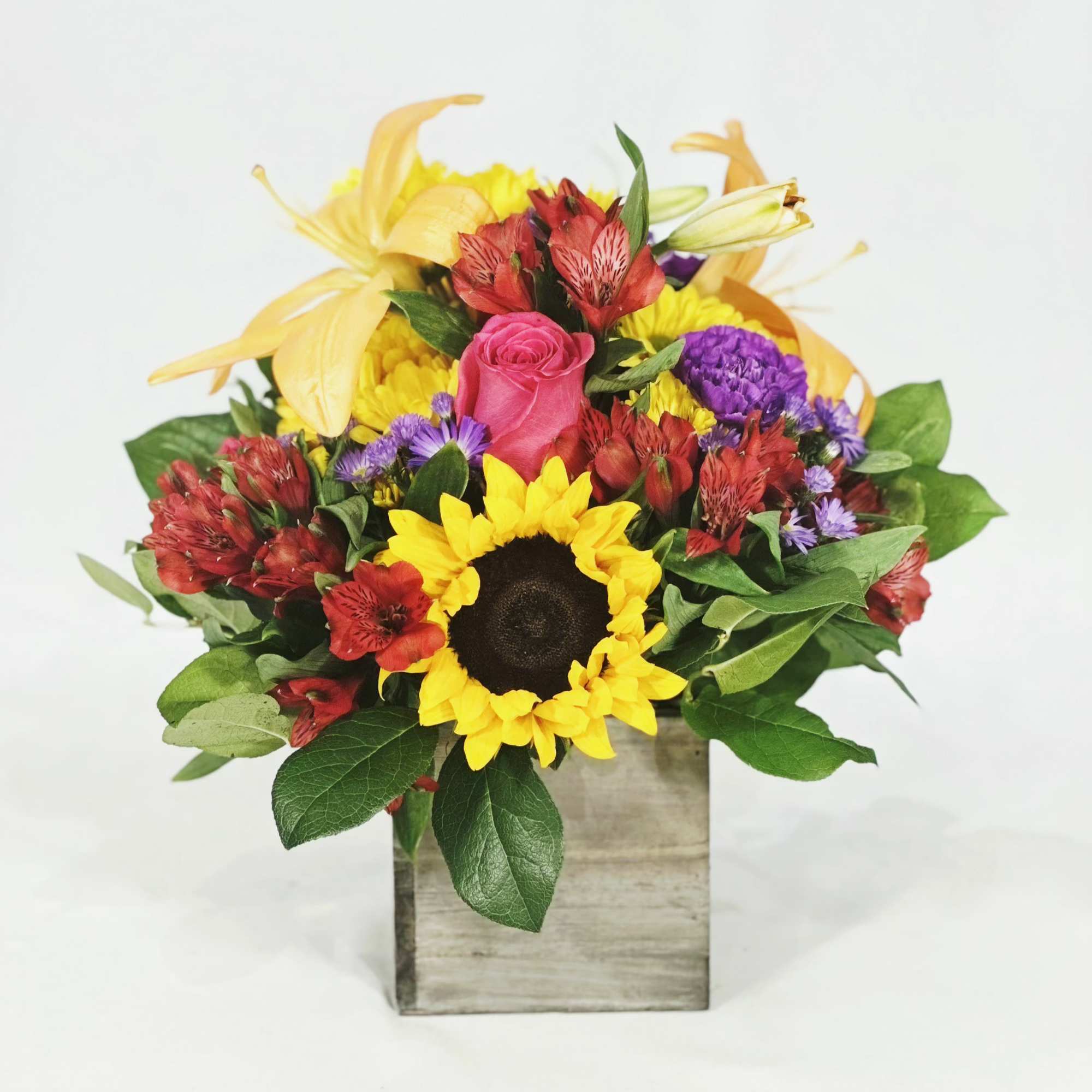 Mixed bouquet with a sunflower, pink rose, and yellow lilies in a wooden box
