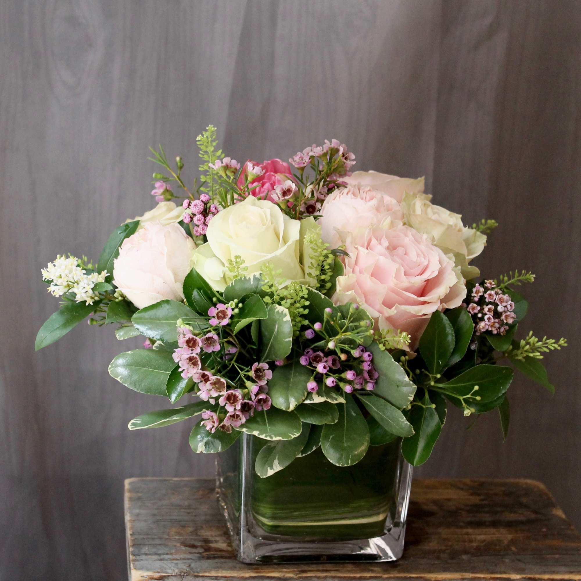 Pink and white roses in a square glass vase with greenery