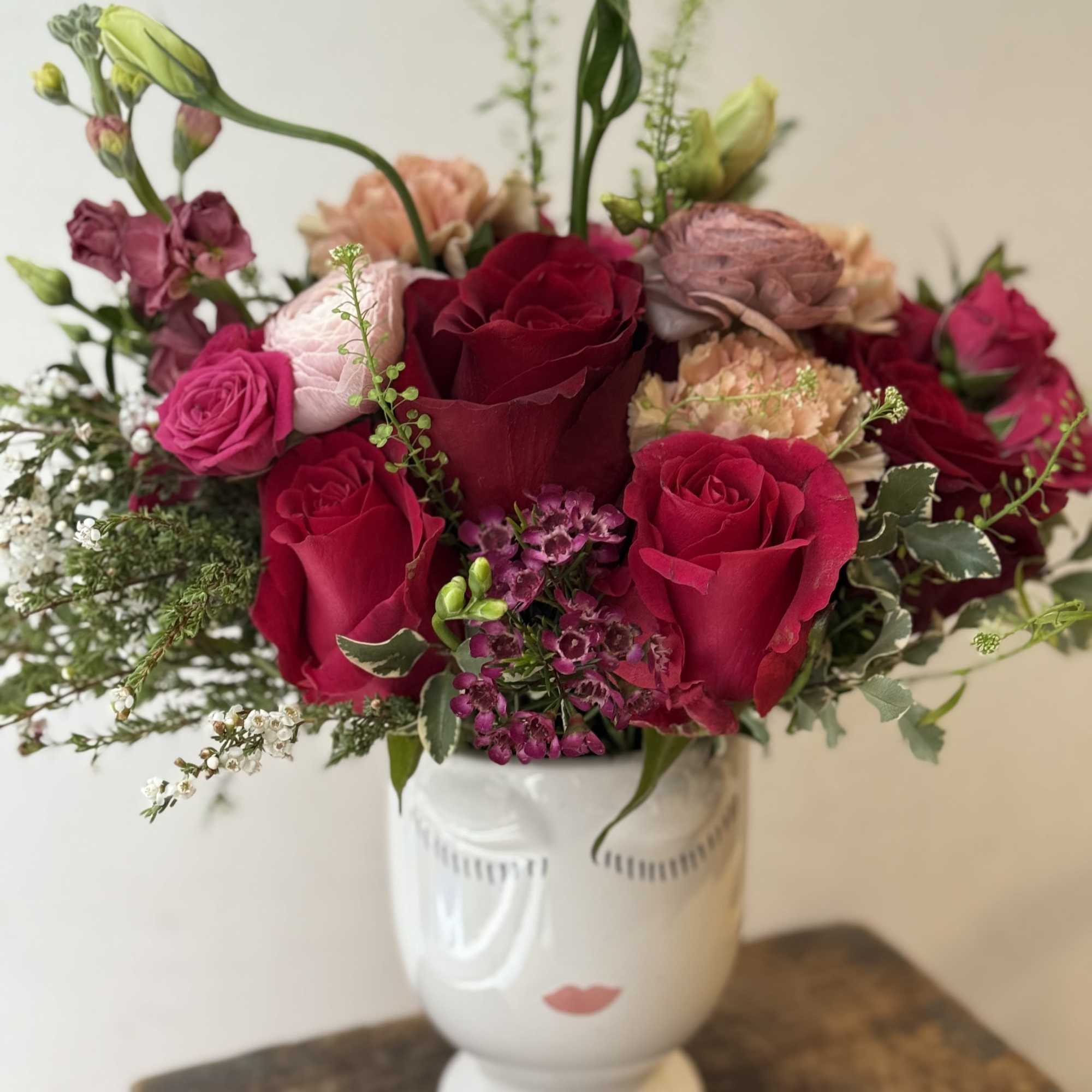 Bouquet of red and pink roses in a white vase with a face design