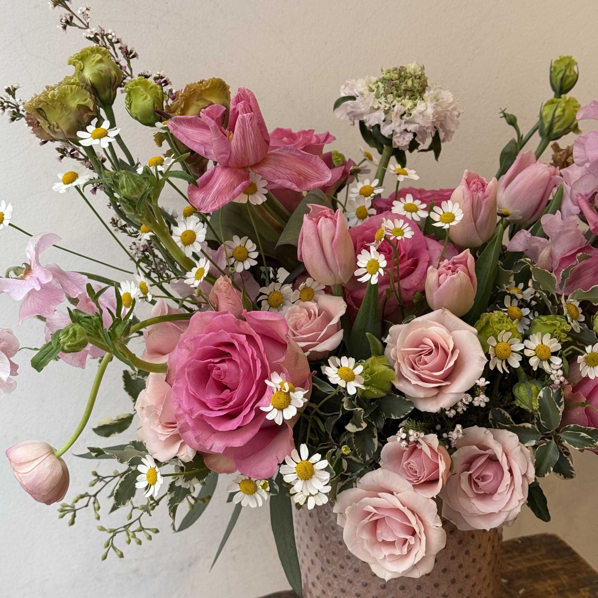 Pink roses and tulips arranged in a textured vase with small white daisies