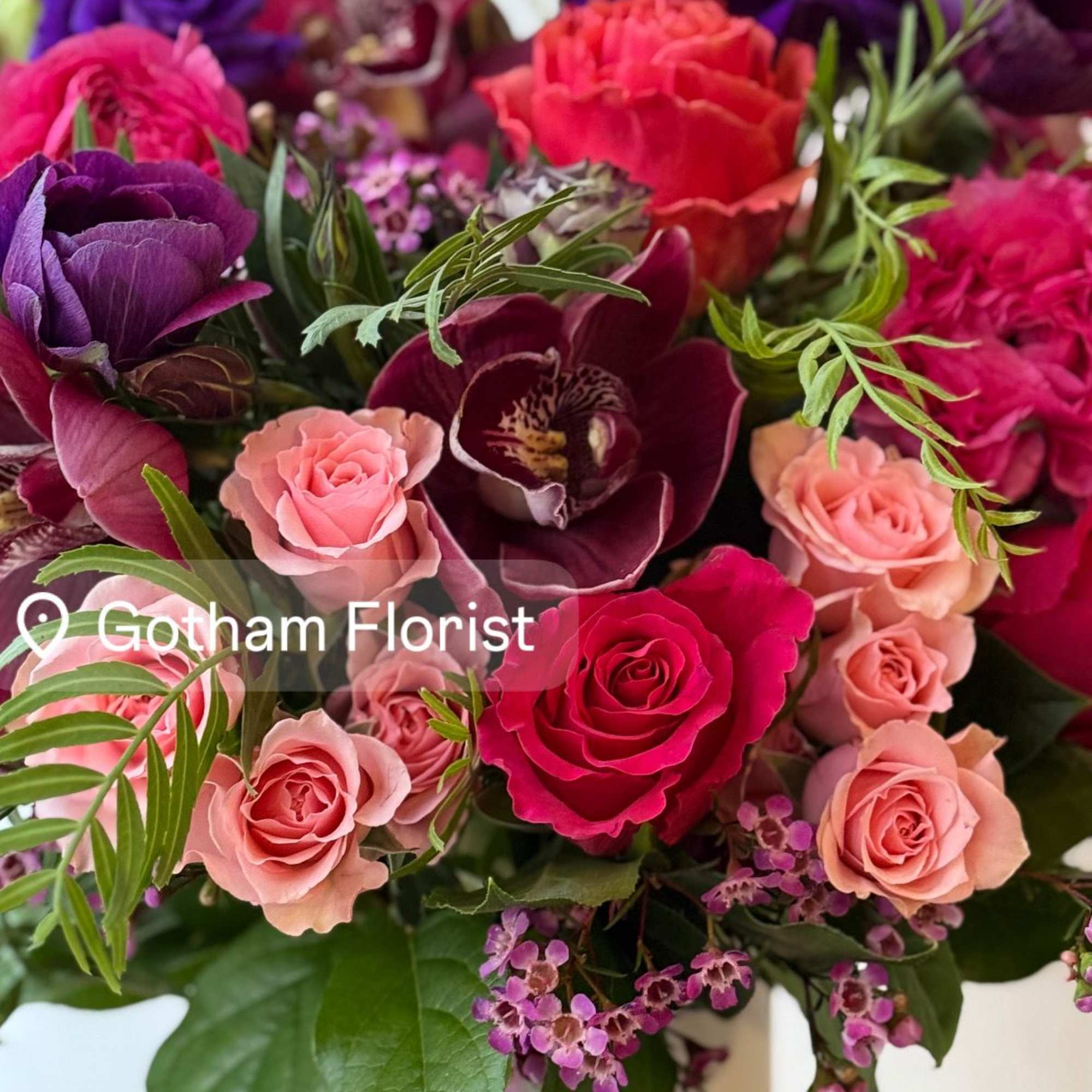 Mixed bouquet of pink, purple, and red flowers in a white vase