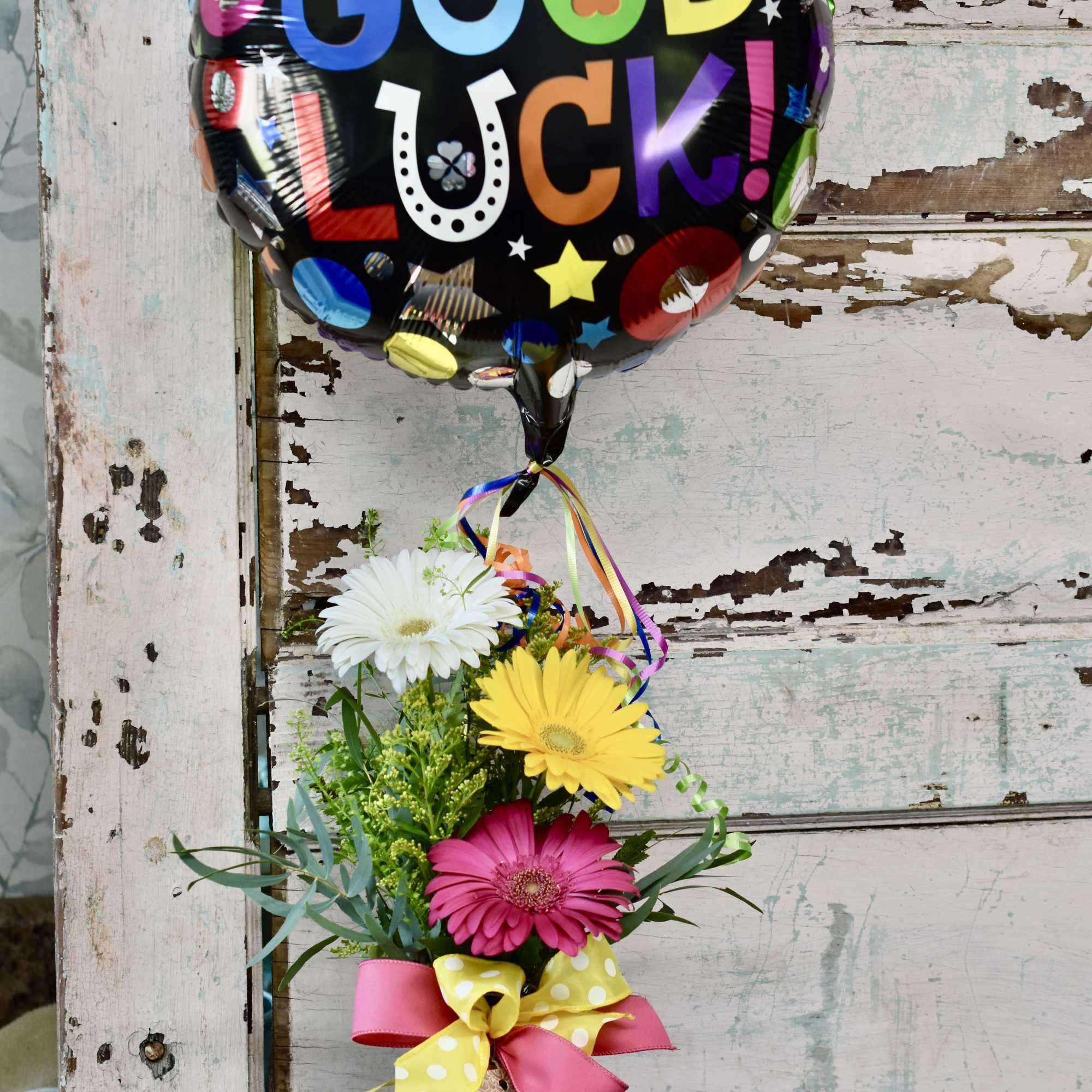 Gerbera bouquet in a glass vase with a "Good Luck" balloon