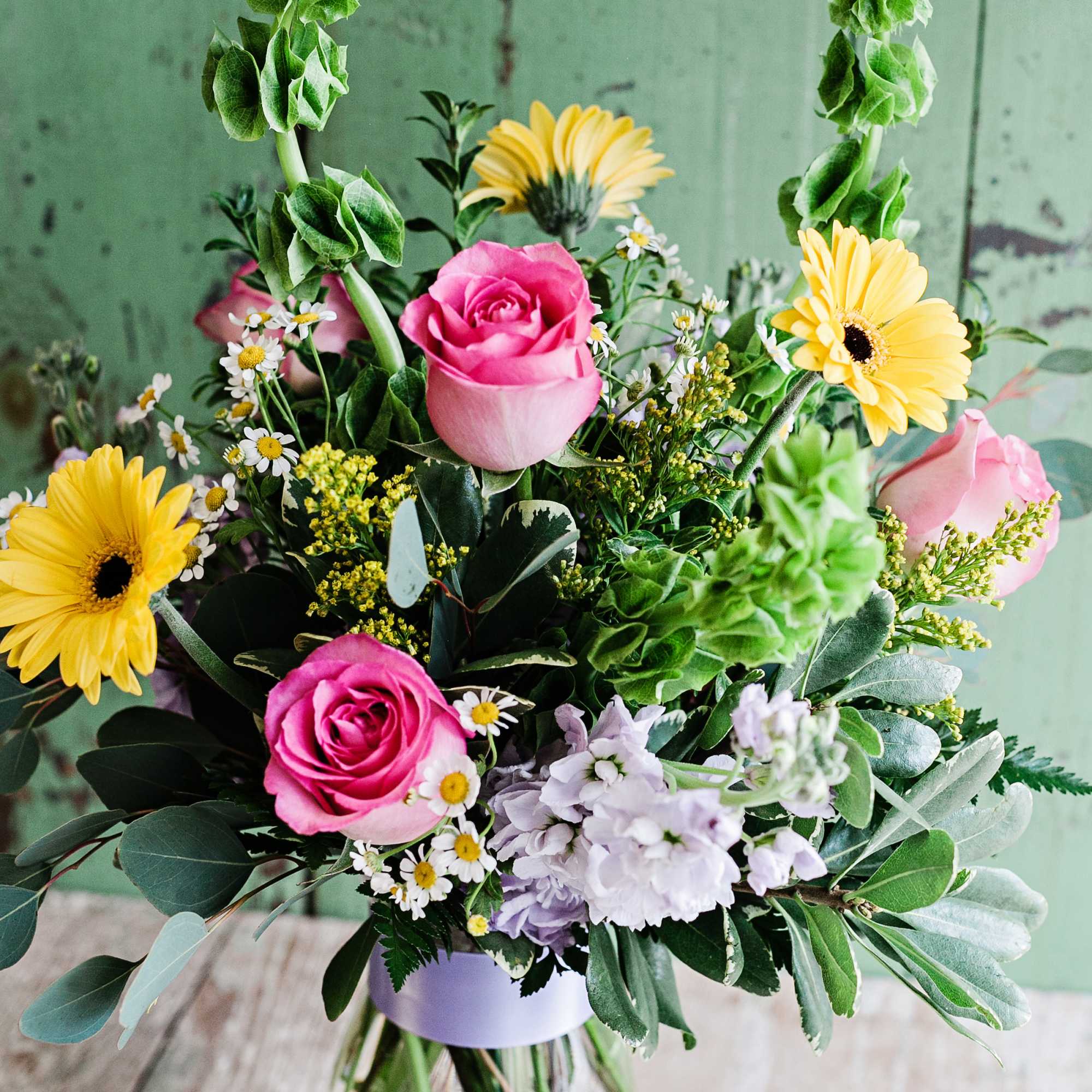 Bouquet of pink roses, yellow gerbera daisies, and lavender flowers in a glass vase