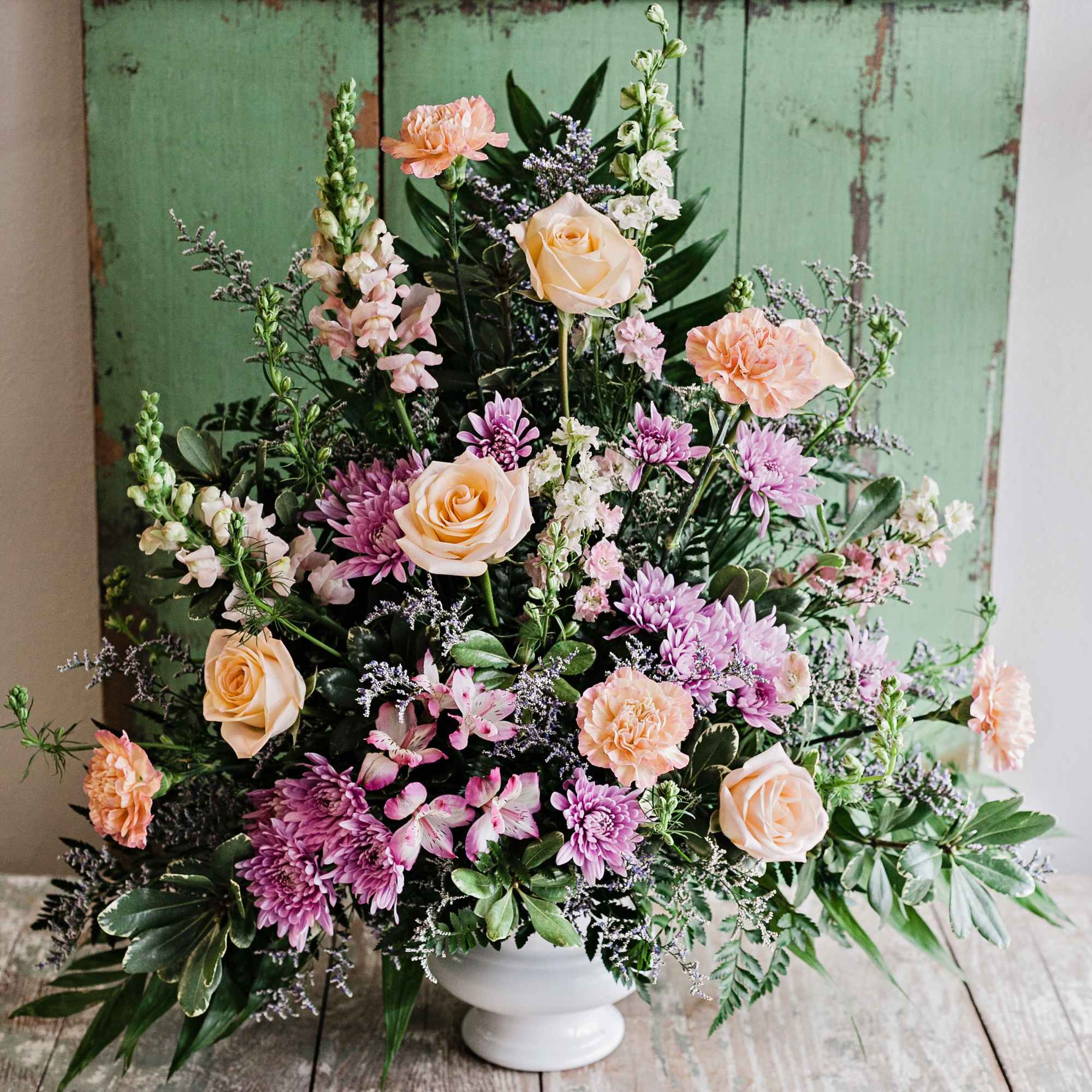 Mixed bouquet of peach roses, pink chrysanthemums, and carnations in a white vase