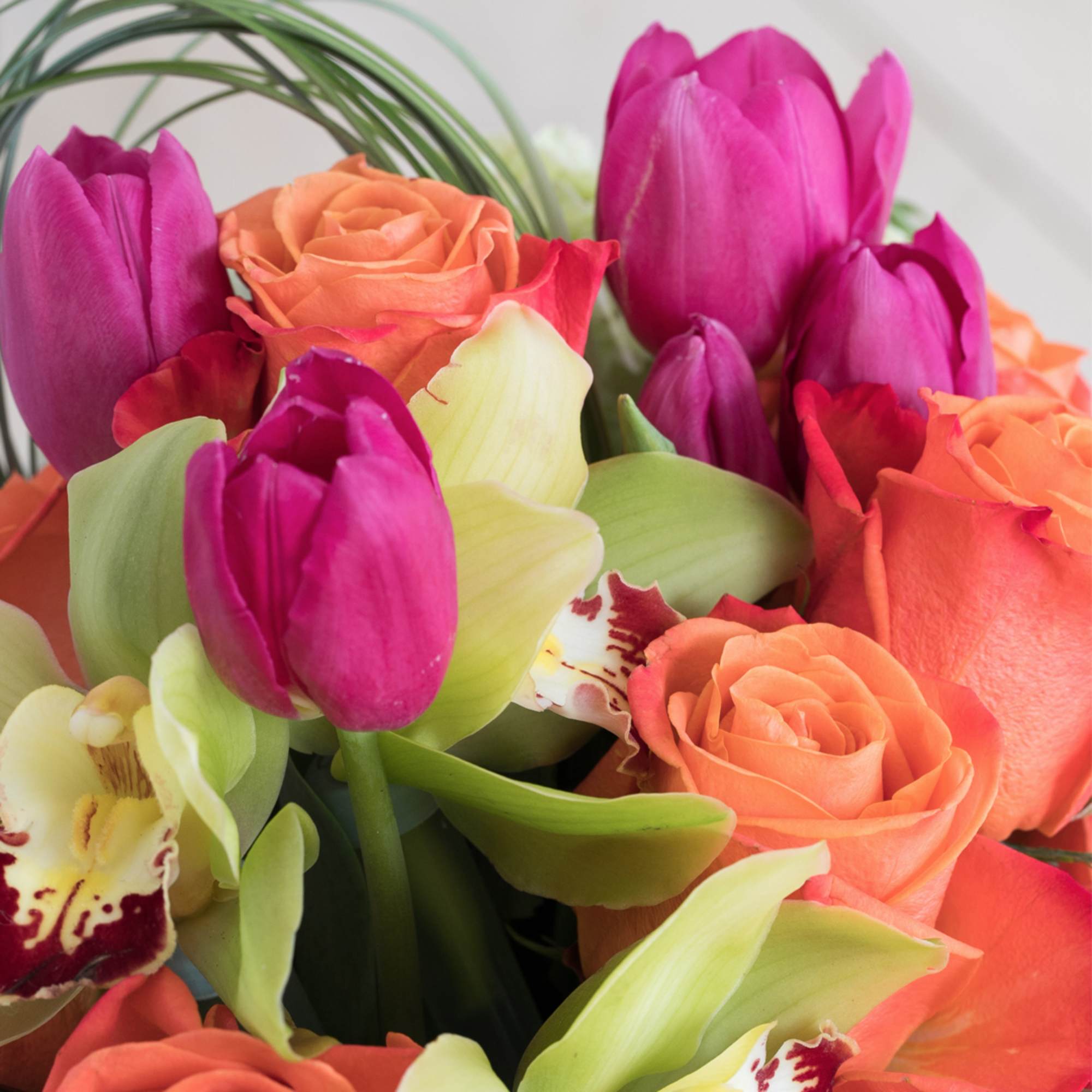 Bright arrangement of hot pink tulips, orange roses, and green orchids in a tight cluster