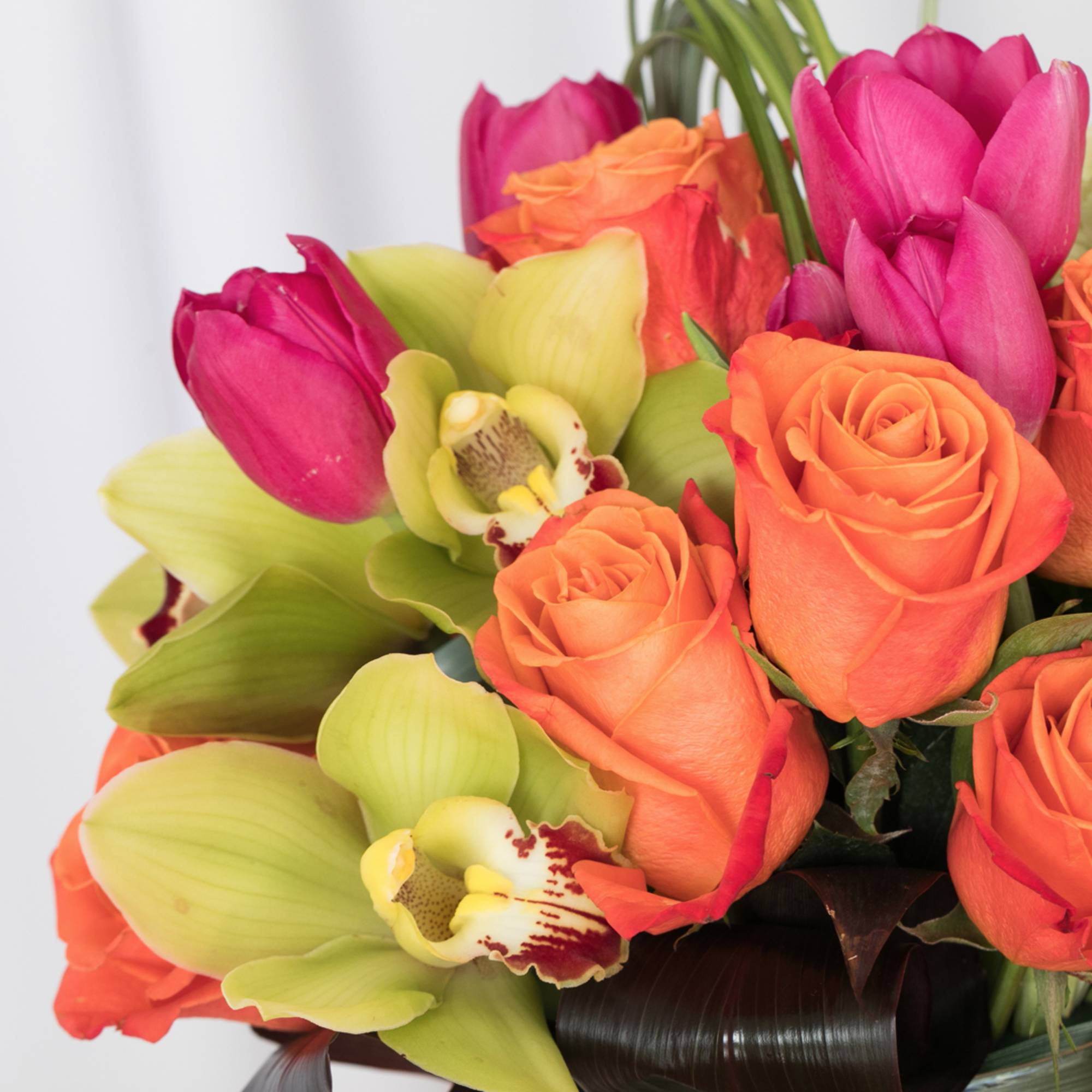 Arrangement of orange roses, pink tulips, and green cymbidium orchids in a compact design