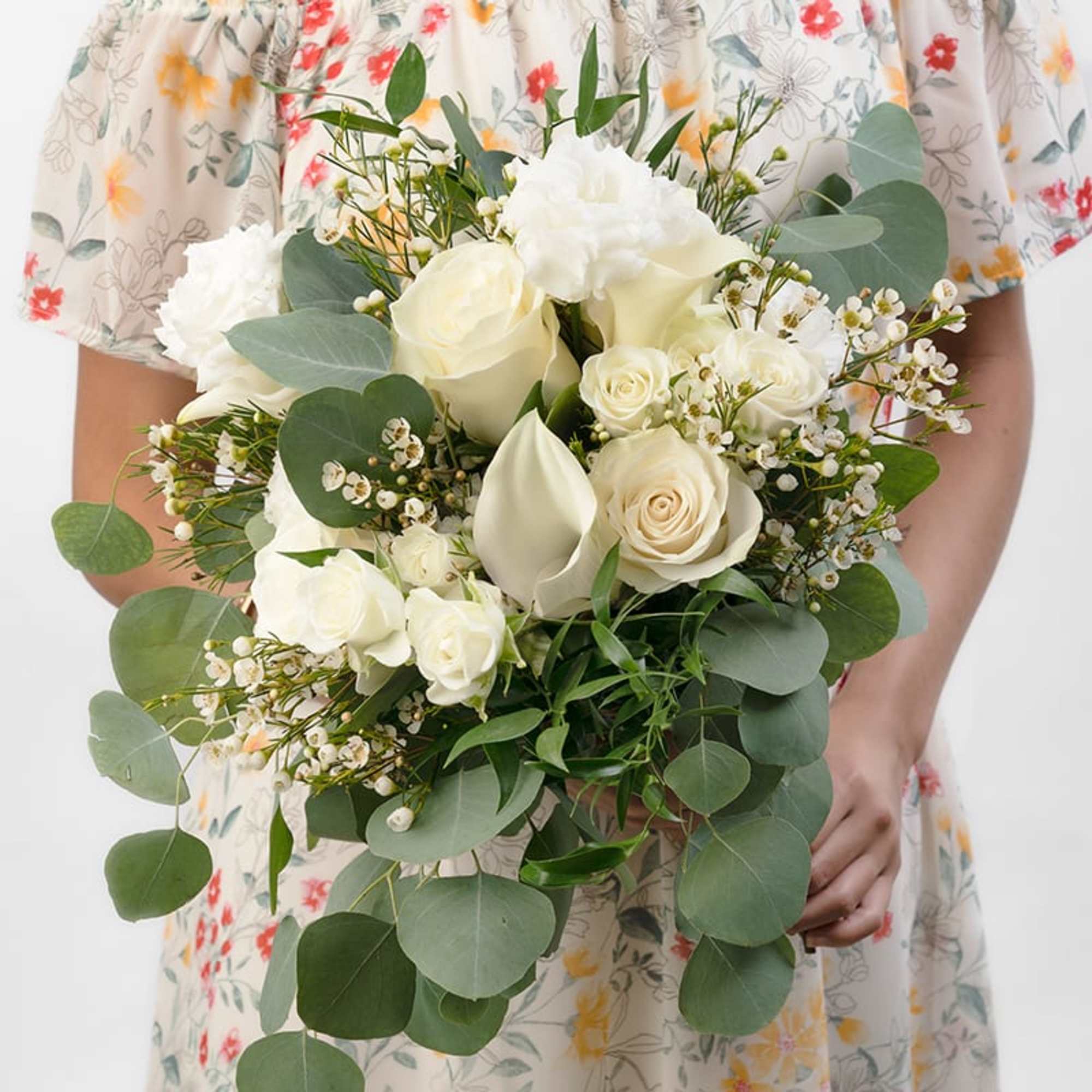 Hand-tied bouquet of white roses, calla lilies, and small white blooms held in front of a floral dress