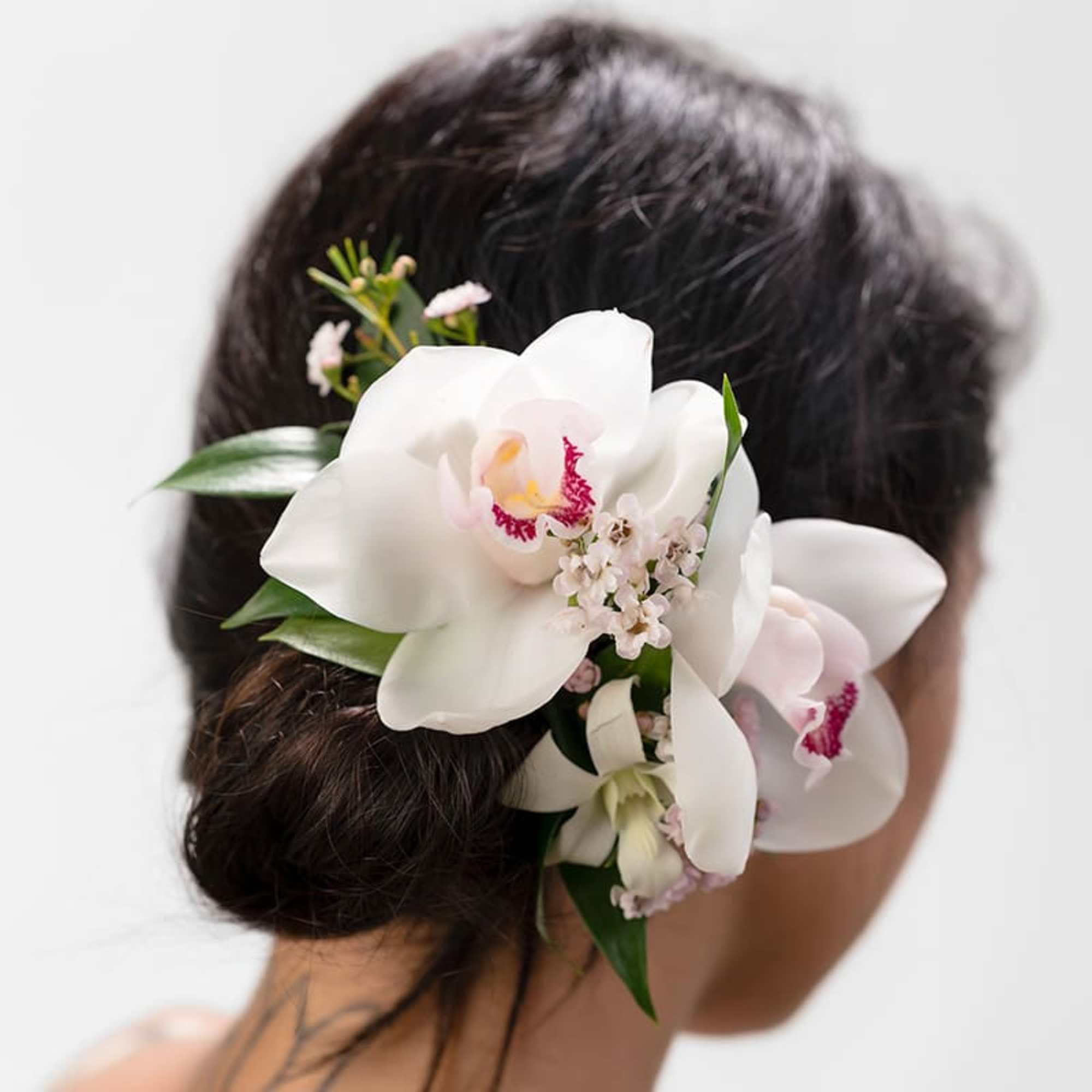 White orchid hair accessory with pink centers worn in a low dark updo from the back.