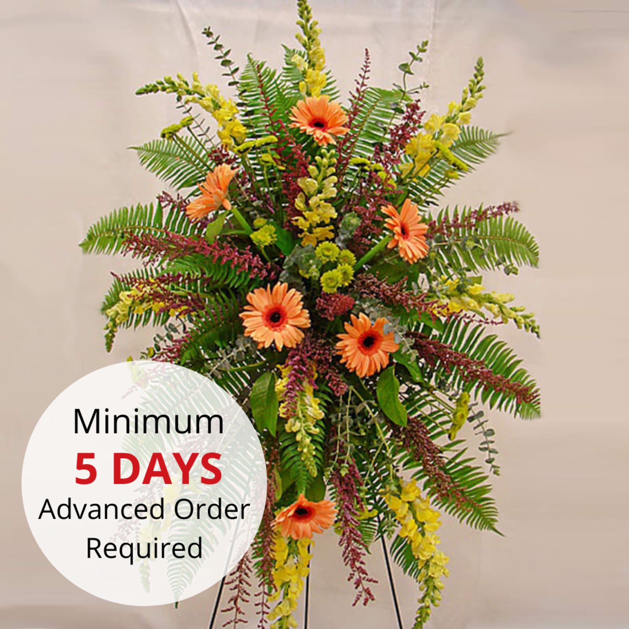 Tall standing spray with orange gerbera daisies, yellow flowers, and ferns on a metal easel