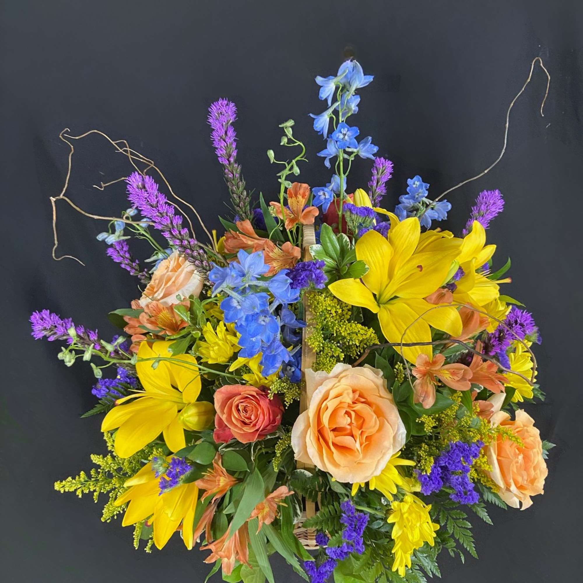 Bright mixed bouquet with yellow lilies, peach roses, and blue flowers