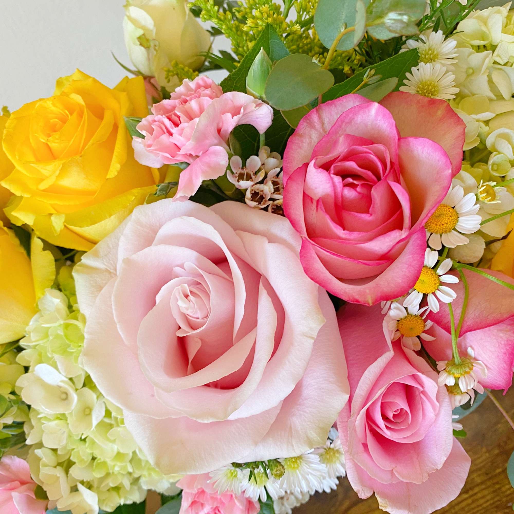 Close-up of a mixed bouquet with yellow and pink roses, hydrangeas, daisies, and carnations.