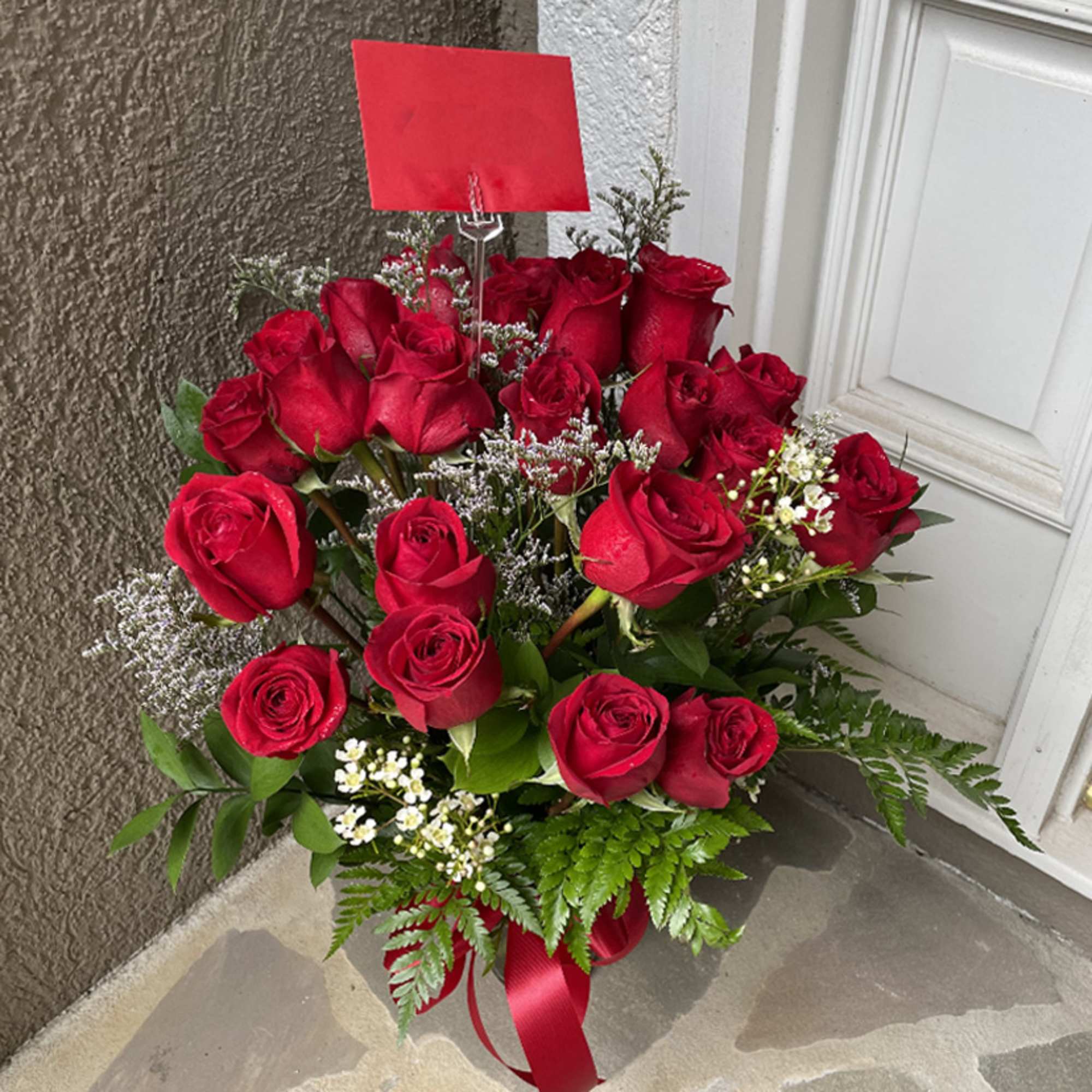 Arrangement of red roses with white filler flowers and a red card on a doorstep