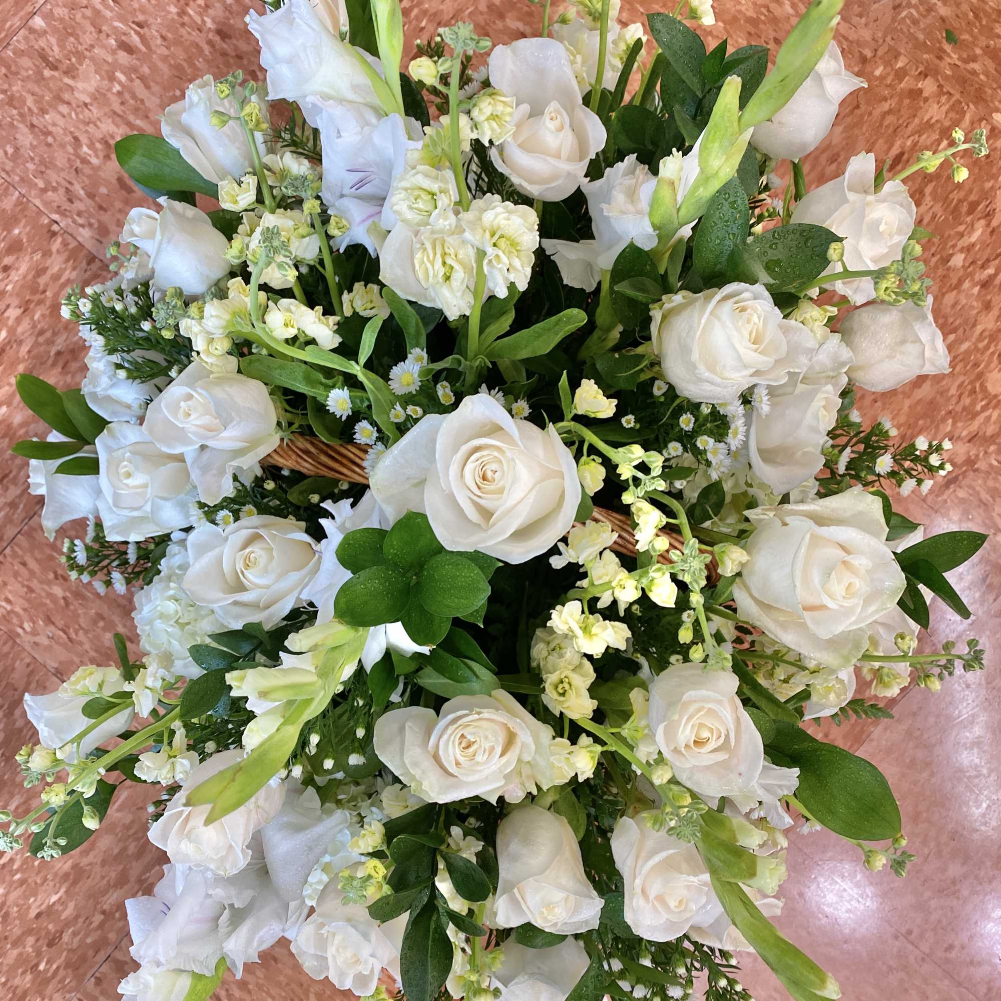 All-white arrangement of roses and other flowers in a wicker basket with abundant foliage