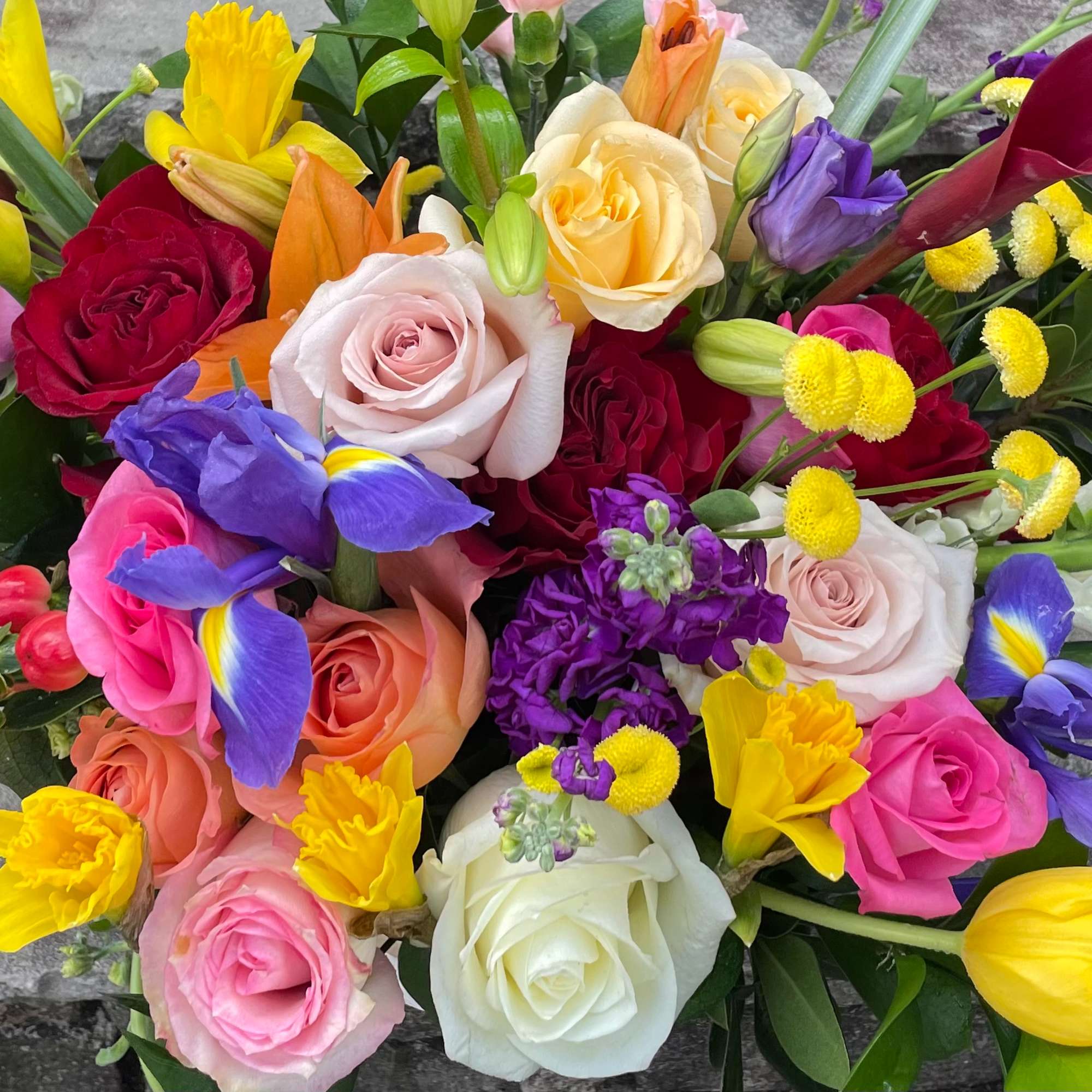 Low arrangement of colorful roses, tulips, irises, and mixed blooms against a stone background