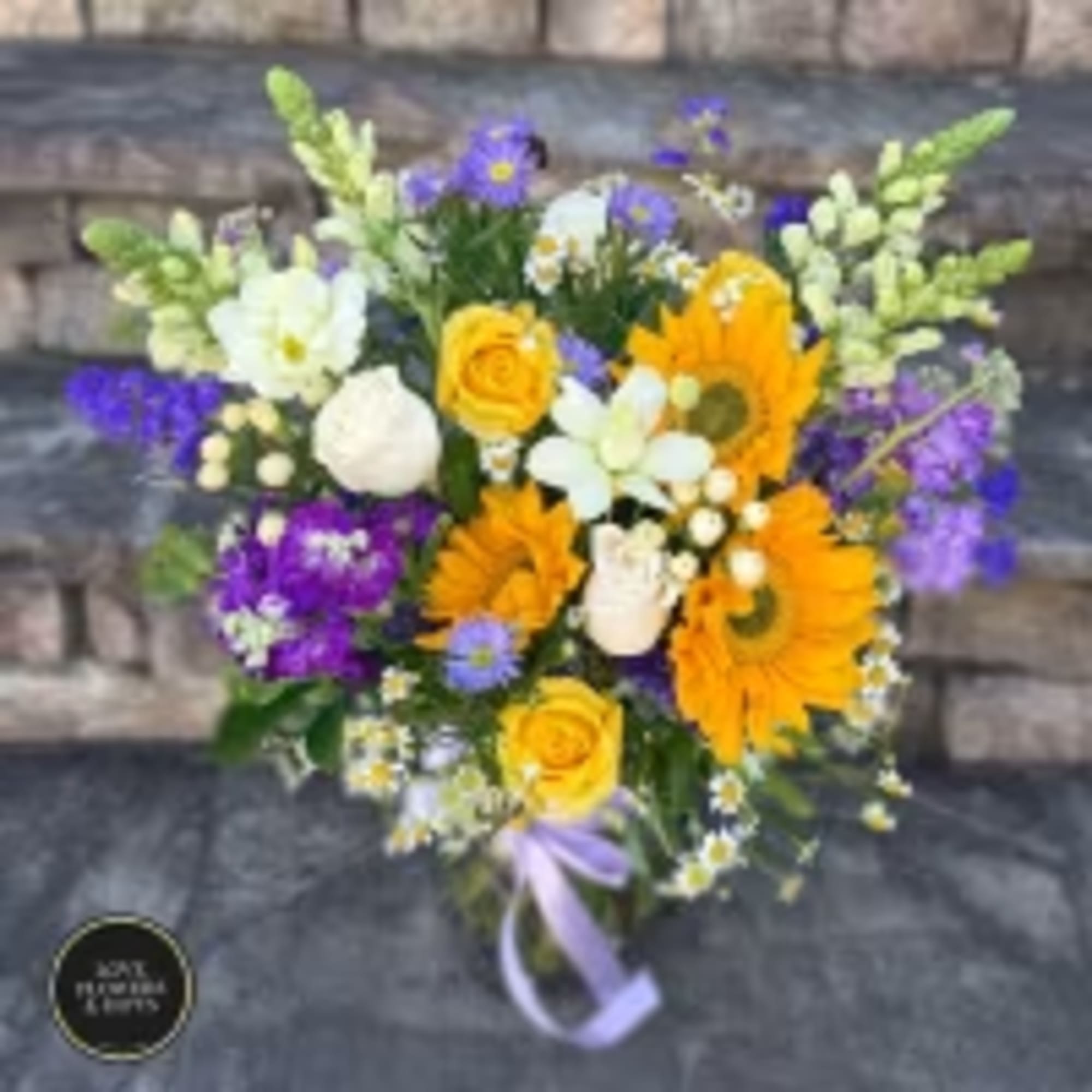 Mixed bouquet of yellow sunflowers, roses, and purple flowers in a clear glass vase