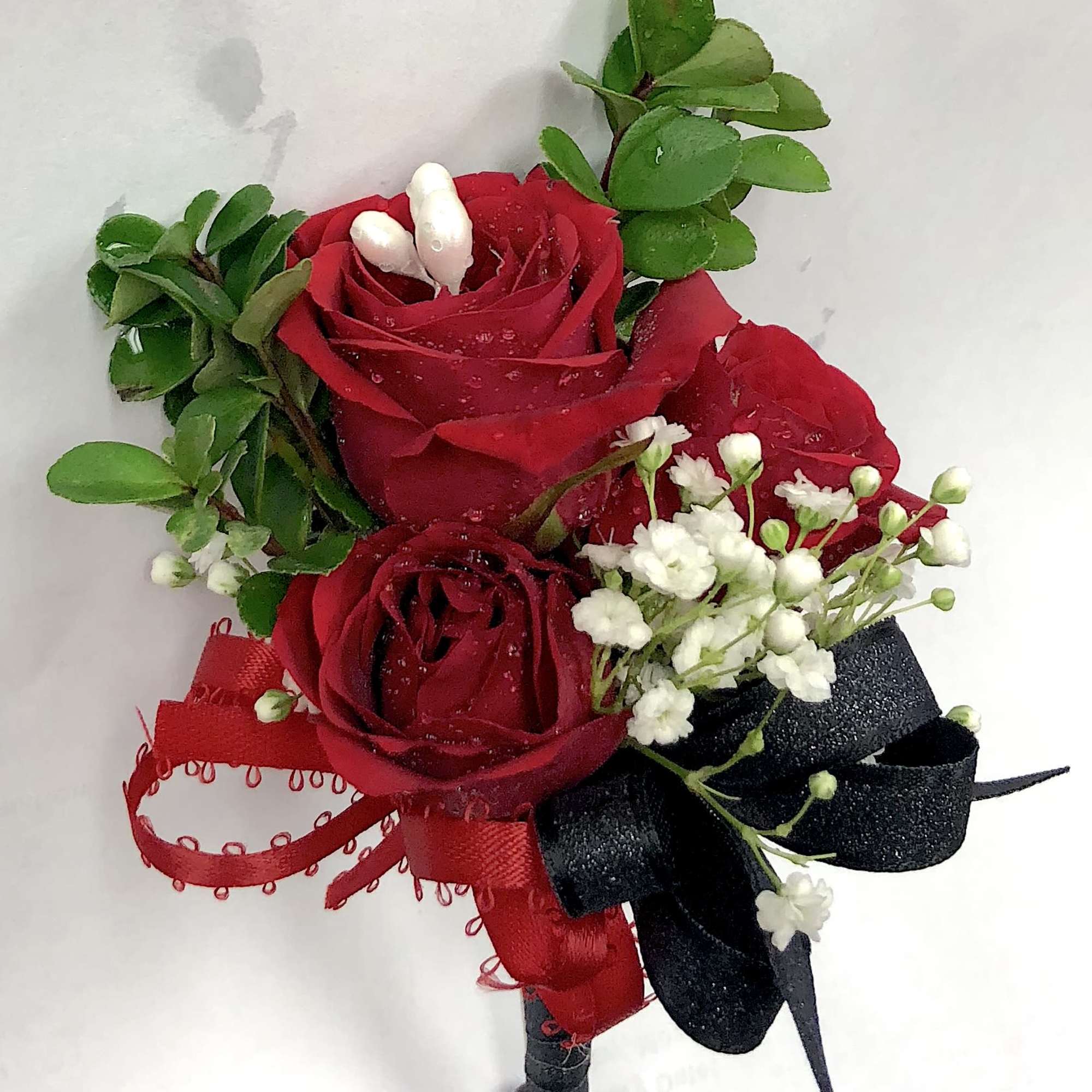 Red rose boutonniere with white filler flowers and red and black ribbons