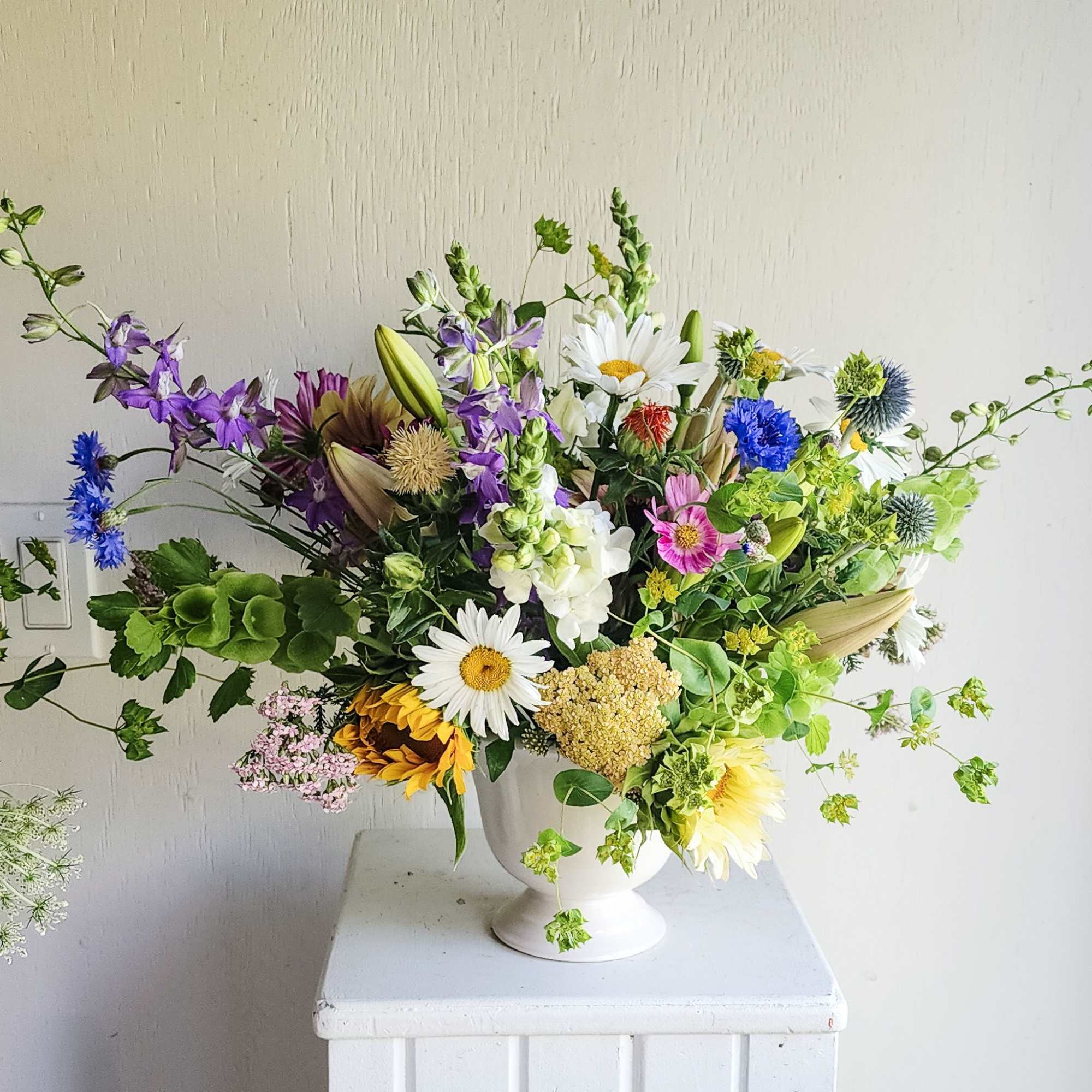 Mixed bouquet in a white pedestal vase with daisies, lilies, and purple blooms