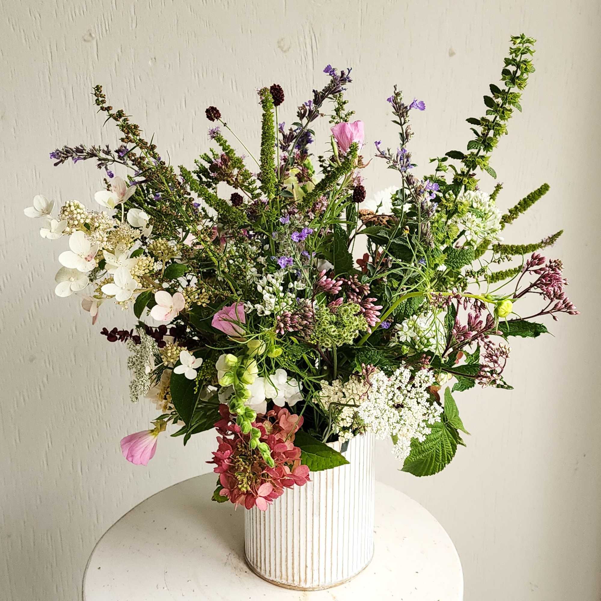 Loose mixed bouquet in a white ribbed vase with pink, white, and purple blooms