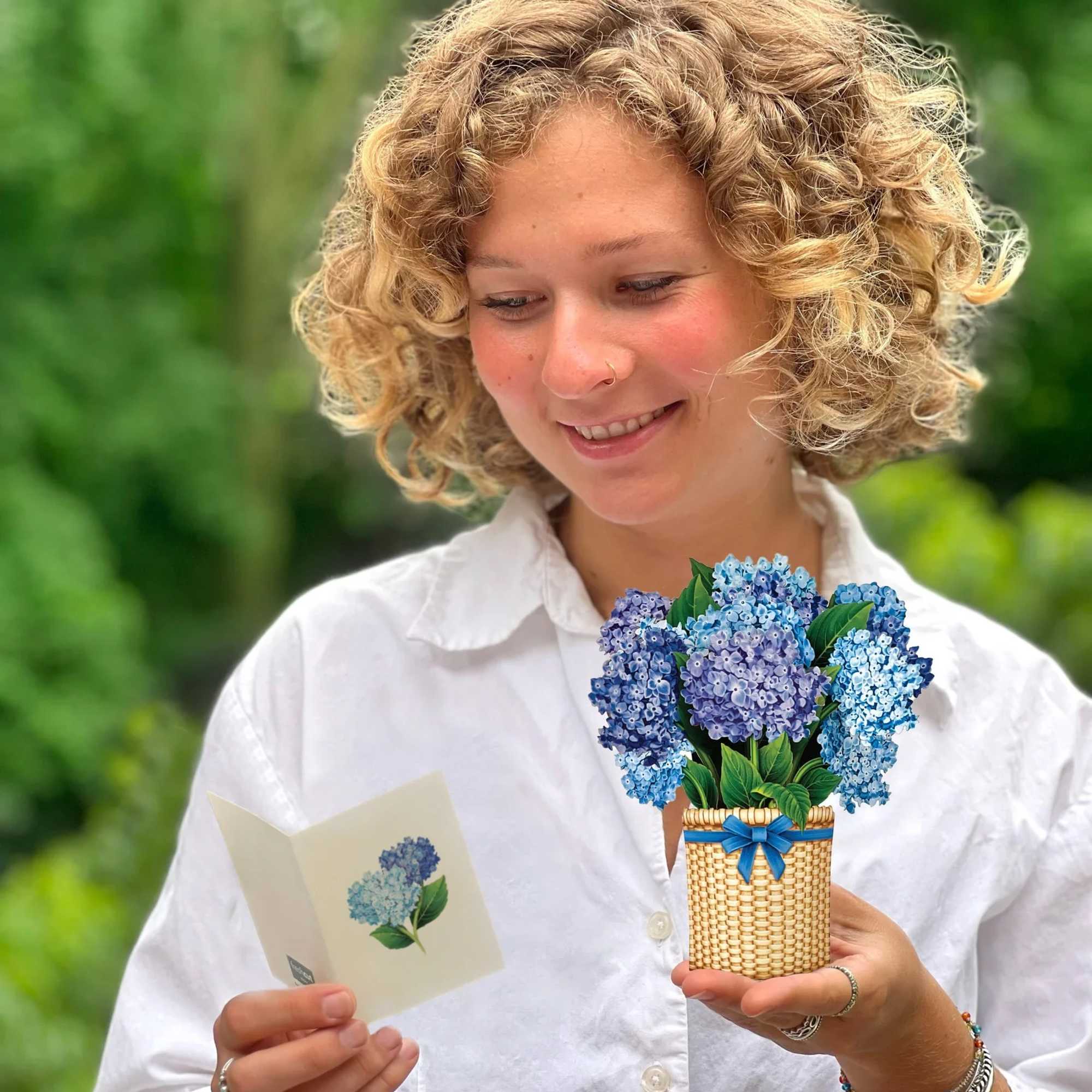 Woman holding a small basket of blue hydrangeas and a matching card